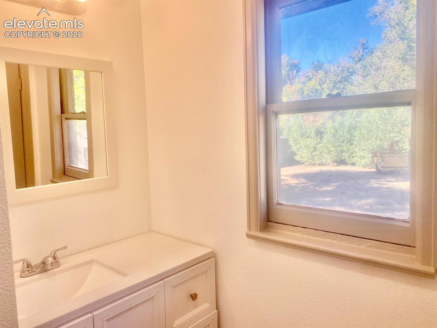 Vanity with integrated sink, dual-handle faucet, framed mirror, and a window with trim