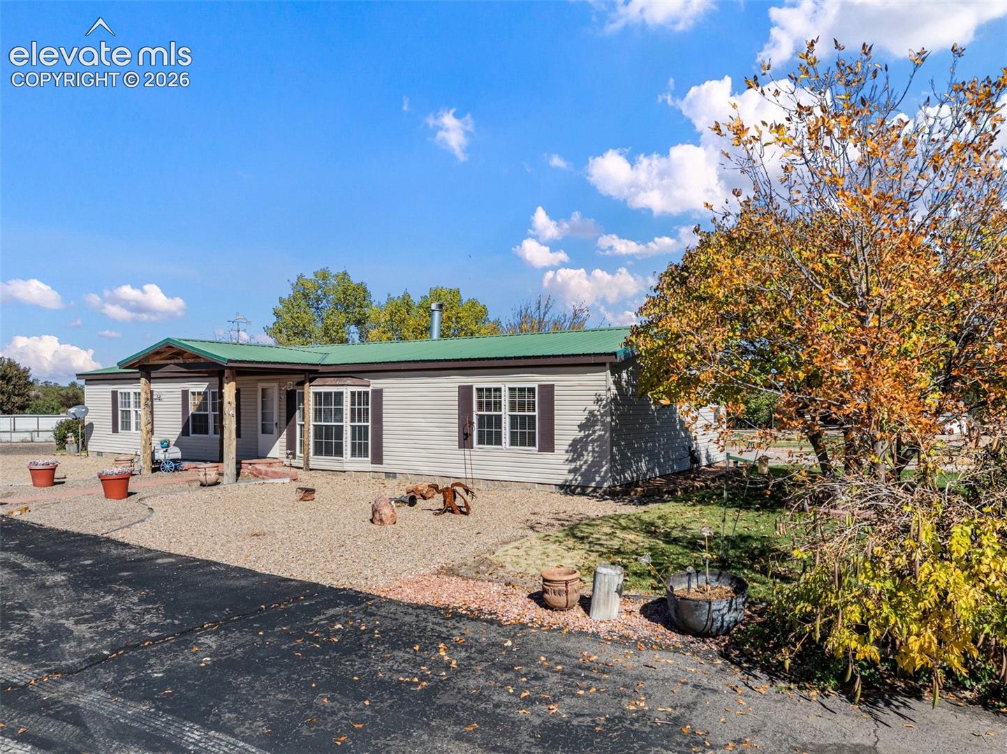 Single-story exterior featuring metal roofing, vinyl siding, a covered entryway with timber posts, and brick paver walkway accents