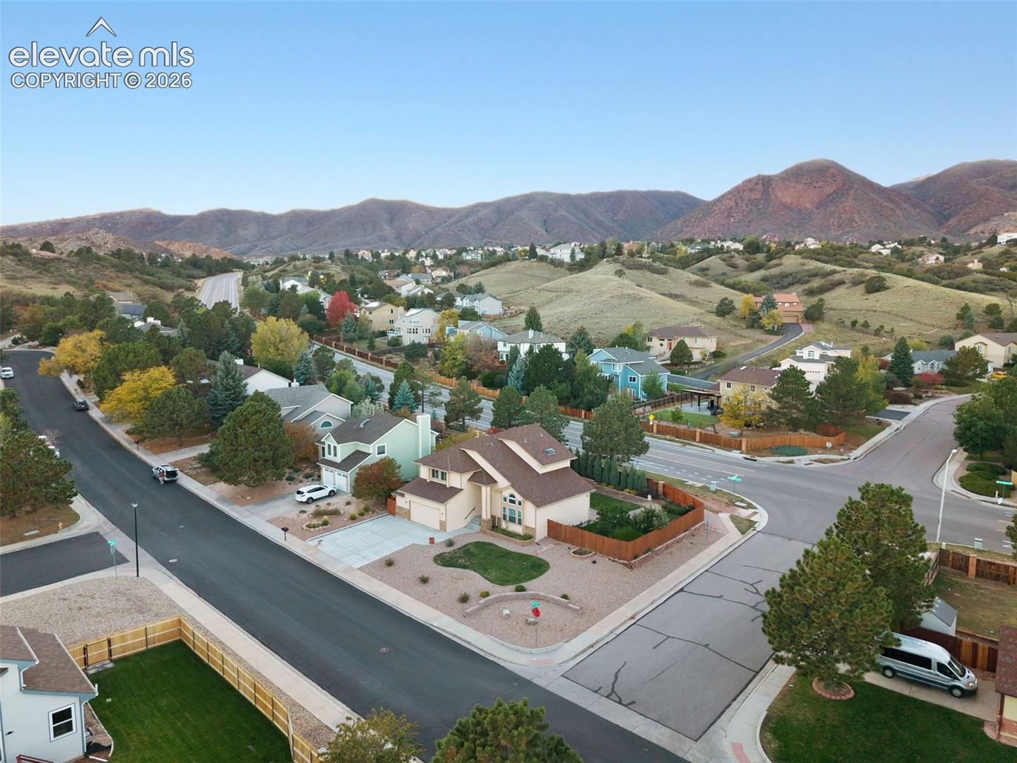 Corner lot residence featuring a multi-level exterior, concrete driveway, stone-accented landscaping, wood privacy fencing, and mountain backdrop