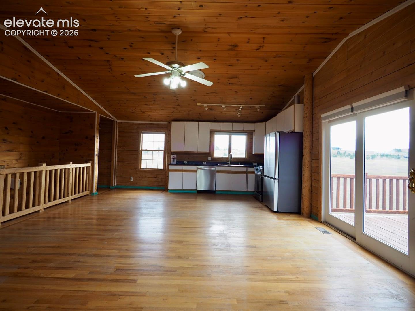 Interior featuring wood-paneled walls and ceilings, wood-finish flooring, white cabinetry with dark countertops, stainless steel appliances, and glass sliding doors