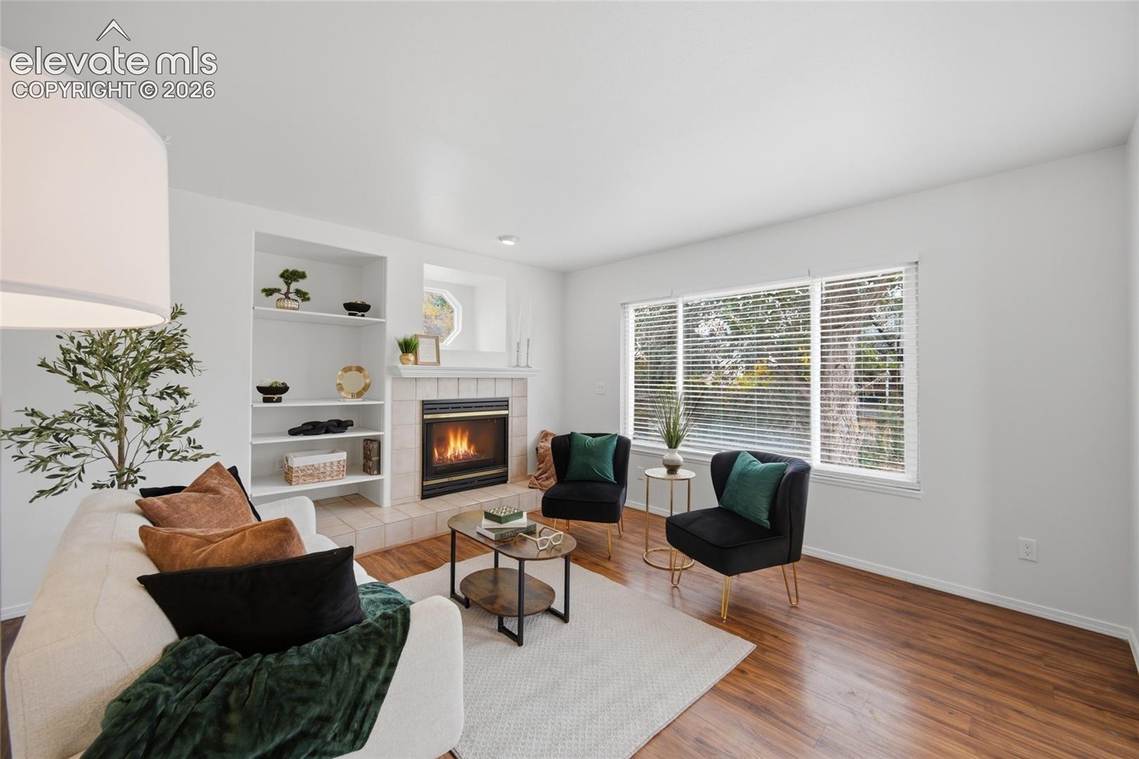 Living area featuring wood-finish flooring, a fireplace with tile surround, built-in recessed shelving, and large windows