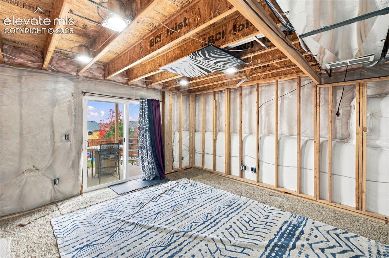 Unfinished lower level featuring exposed wood joist ceilings, metal-framed wall studs, vapor barrier insulation, and a sliding glass door