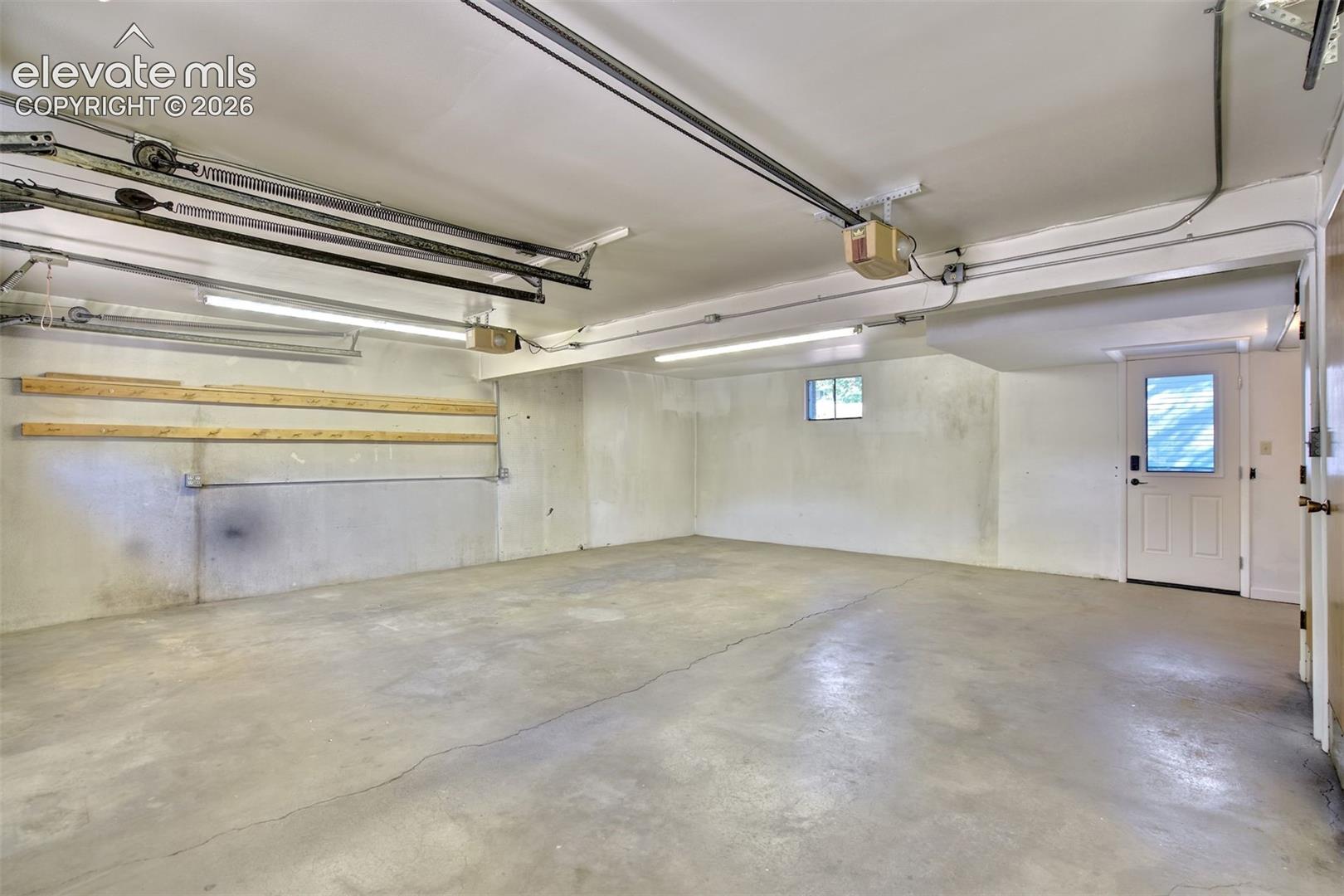 Garage space featuring concrete flooring, overhead lighting, built-in wooden wall shelving, and an exterior access door with a windowed panel
