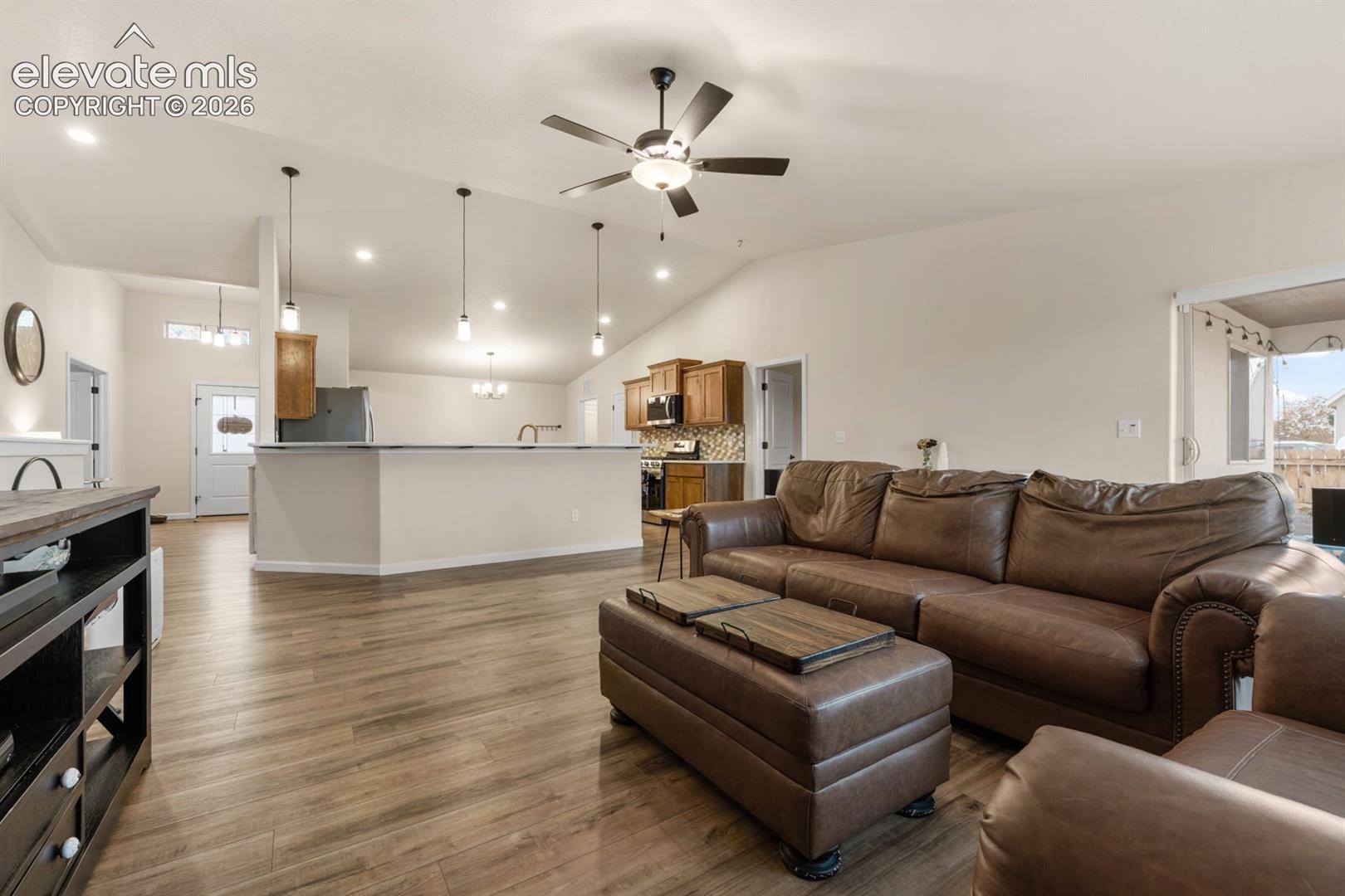 Open-concept interior featuring vaulted ceilings, wood-finish flooring, recessed lighting, and a multi-pendant island fixture