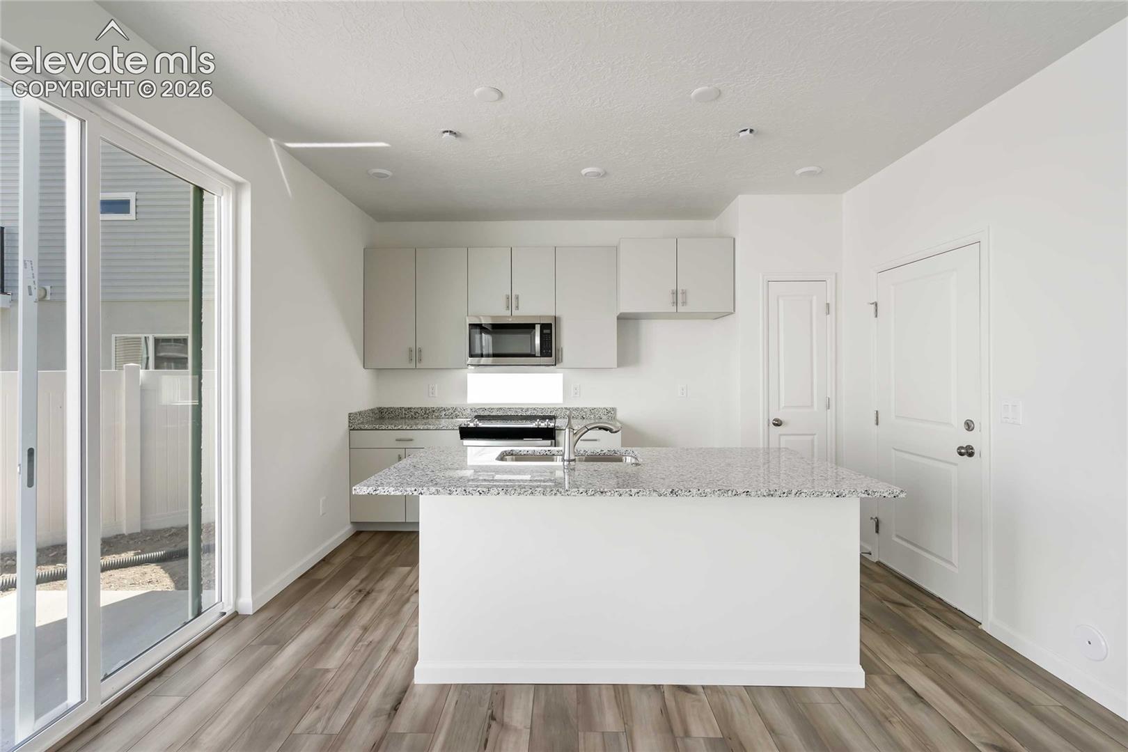 Kitchen featuring a central island with an integrated sink, light-toned cabinetry, stainless steel appliances, and granite-look countertops
*photos of a model home*