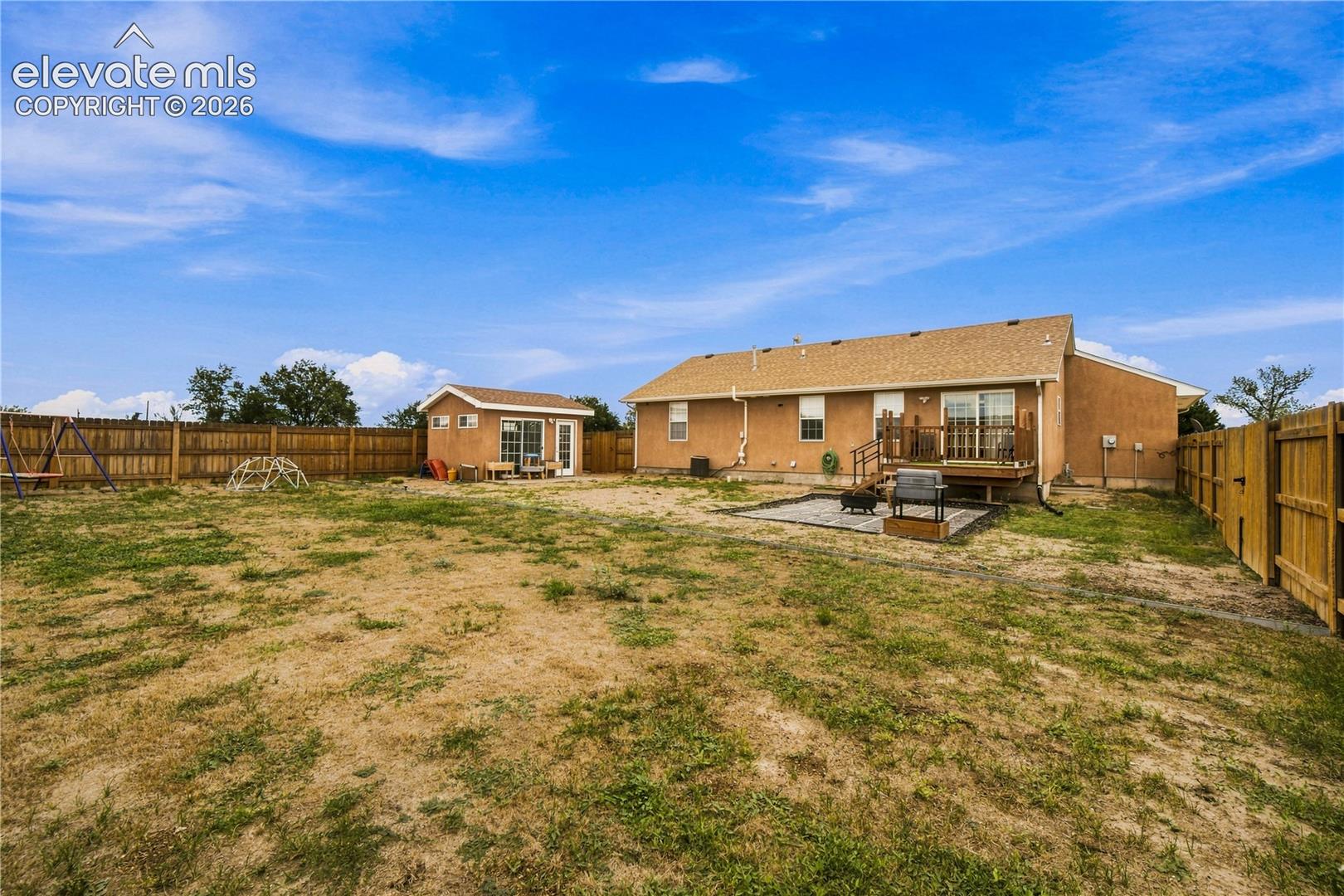 Expansive backyard with a wood privacy fence, detached outbuilding, wood deck, and a paved patio area
