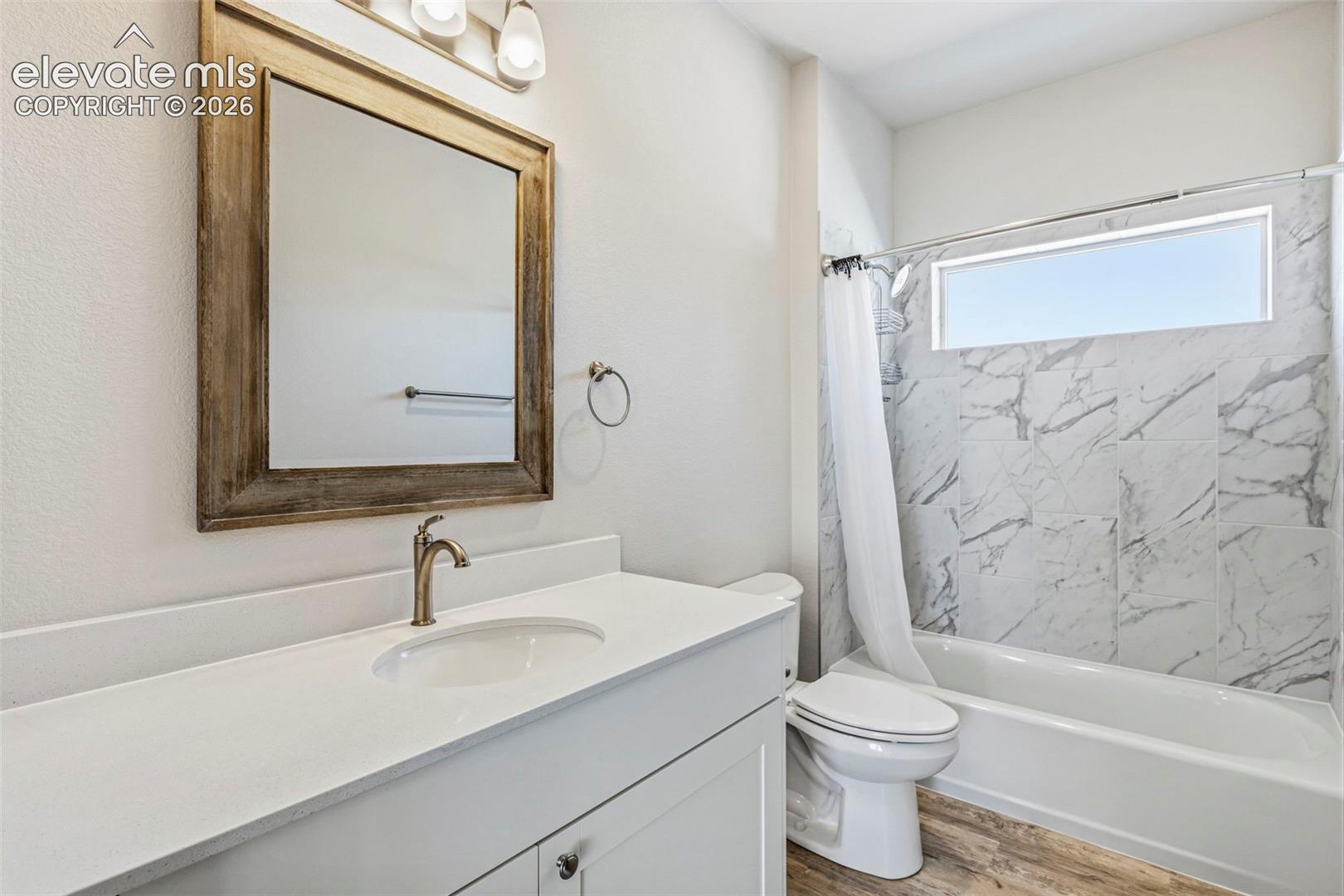 Bathroom featuring a white vanity with an integrated sink, brushed bronze faucet, and a framed mirror