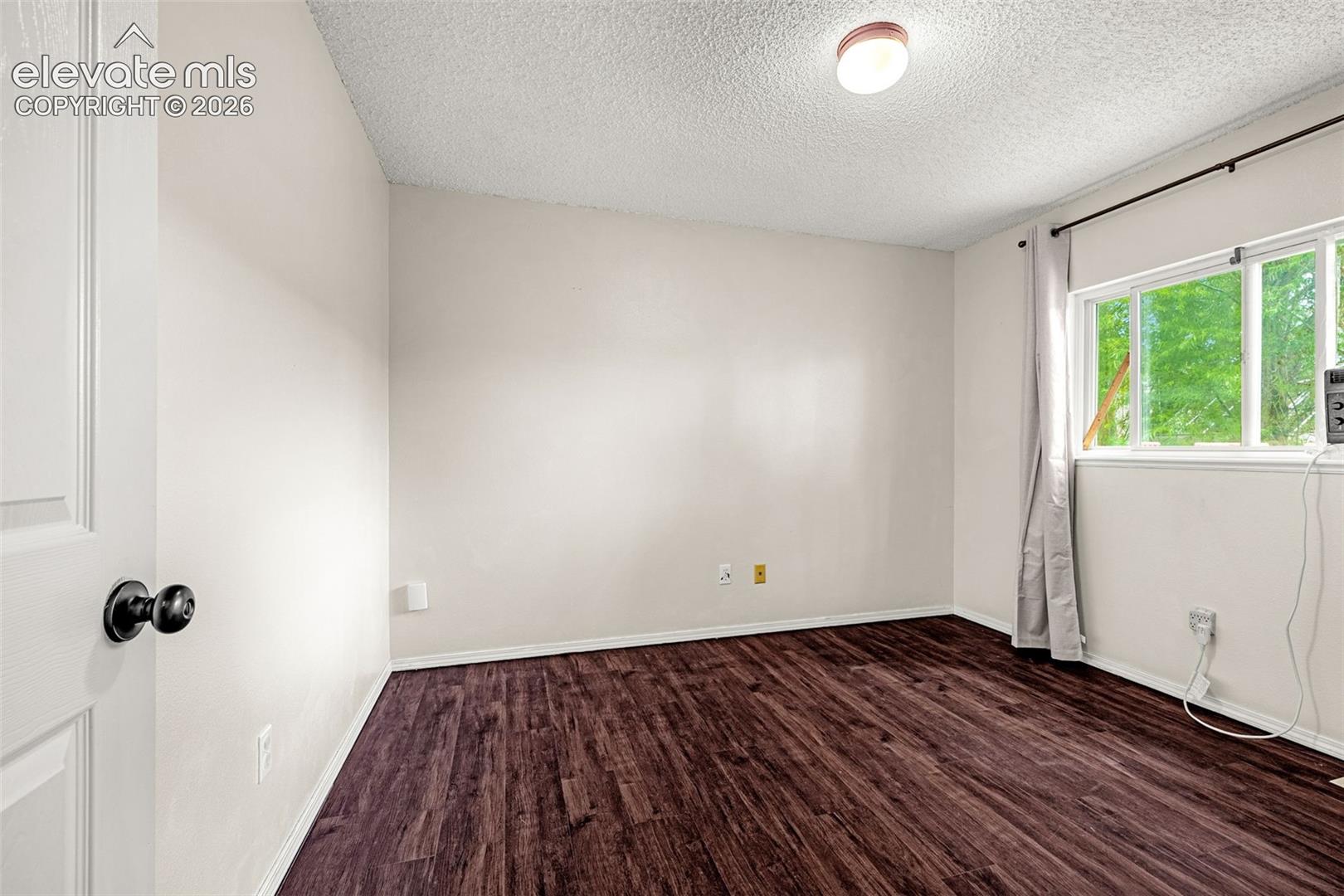 Bright bedroom featuring luxury vinyl wood-look flooring, white walls, and a window with outdoor tree scenery