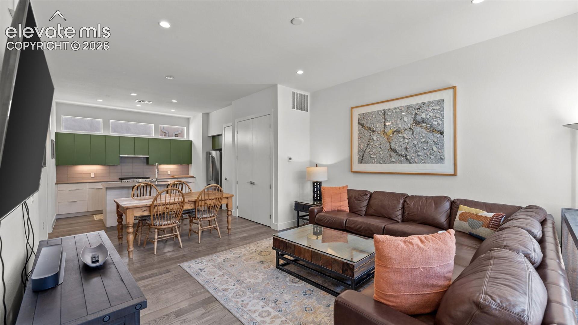 Open-concept interior featuring wood-finish flooring, recessed lighting, and a kitchen equipped with green upper cabinetry, a kitchen island, and light-toned lower cabinetry