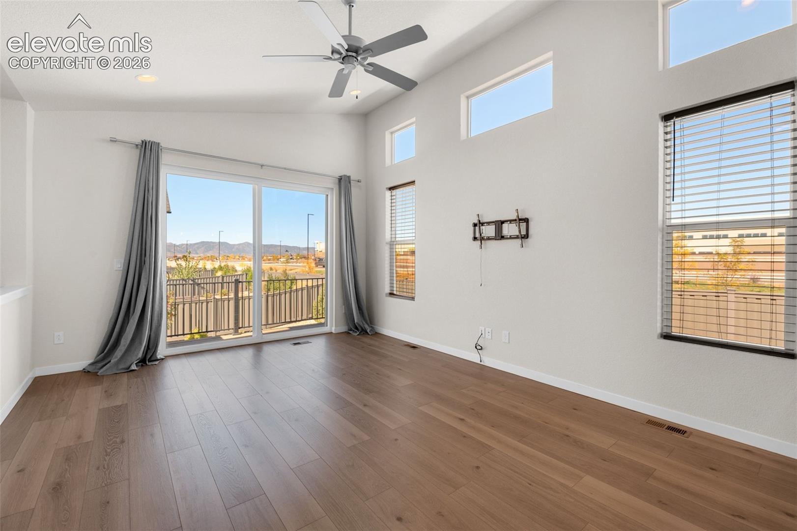 Living area featuring high vaulted ceilings, wood-finish flooring, sliding glass door, tiered transom windows, and a ceiling fan