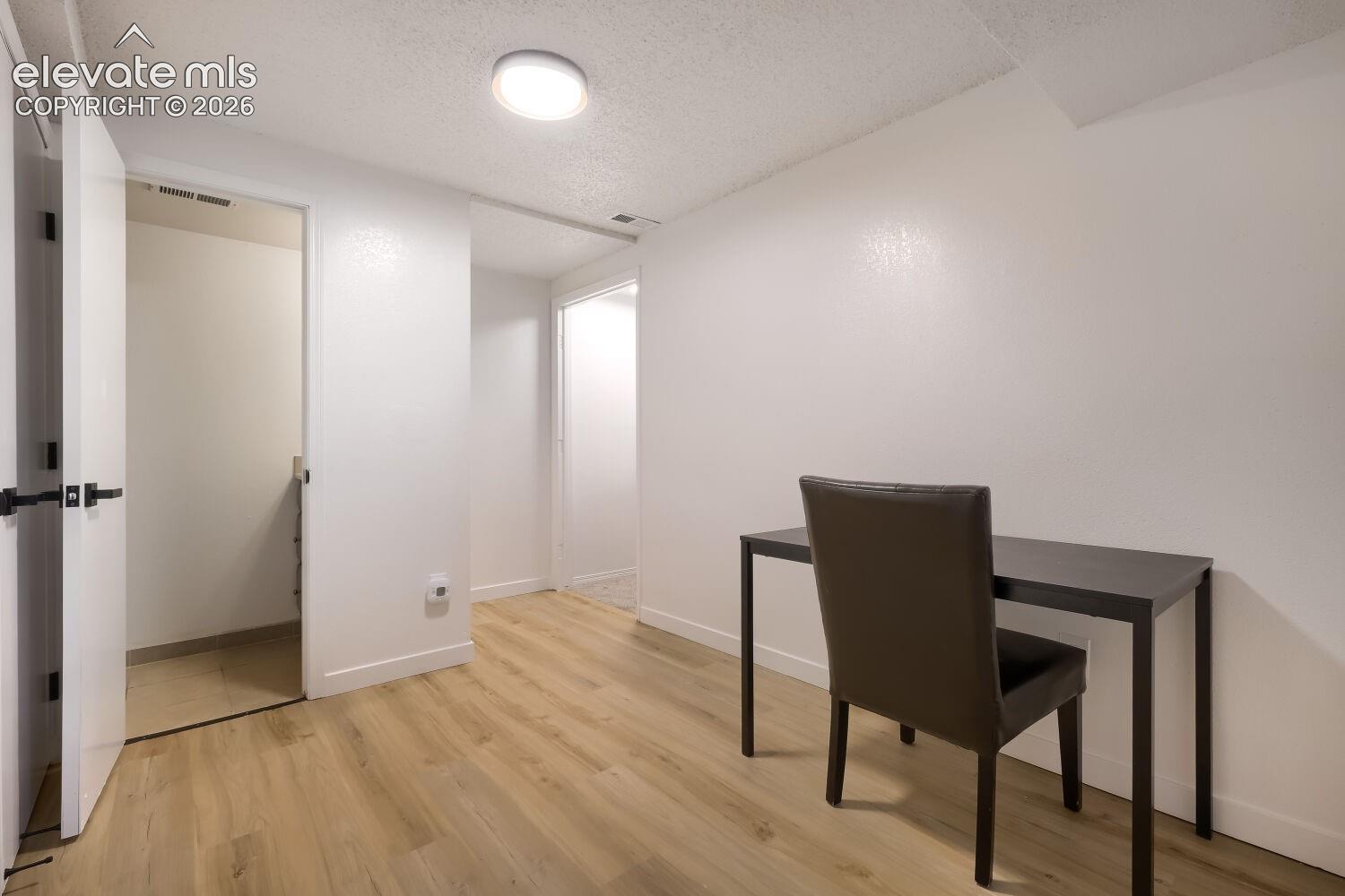 Interior space featuring neutral wall tones, light wood-finish flooring, ceiling-mounted lighting, and matte black door hardware