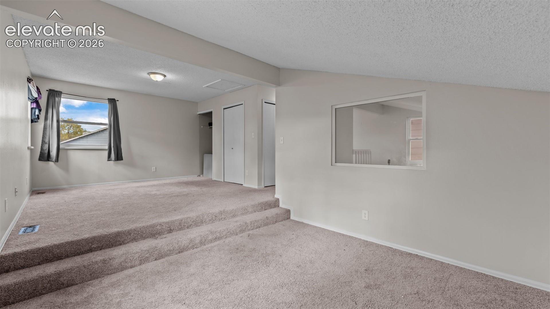 Multi-level room featuring wall-to-wall carpeting, vaulted ceilings, and a framed interior cutout