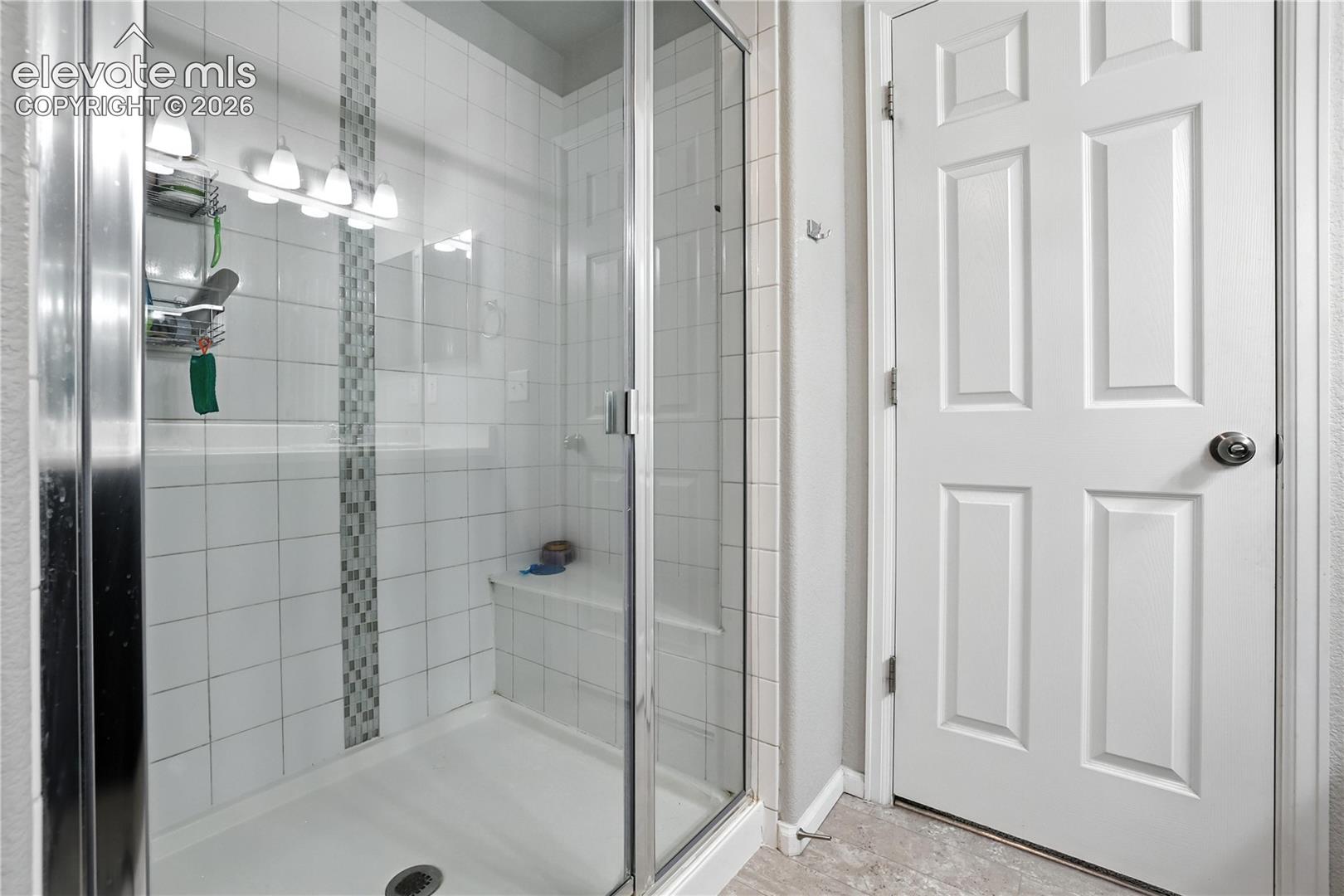 Glass-enclosed shower with a built-in bench, white tile surround, and decorative mosaic accent strip