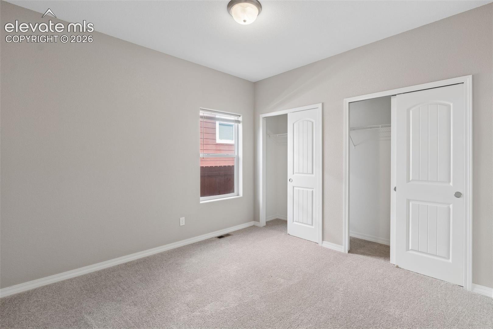 Main Level Bedroom #2 Carpeted room with a ceiling-mounted light fixture, a single window, and two bi-fold closet doors