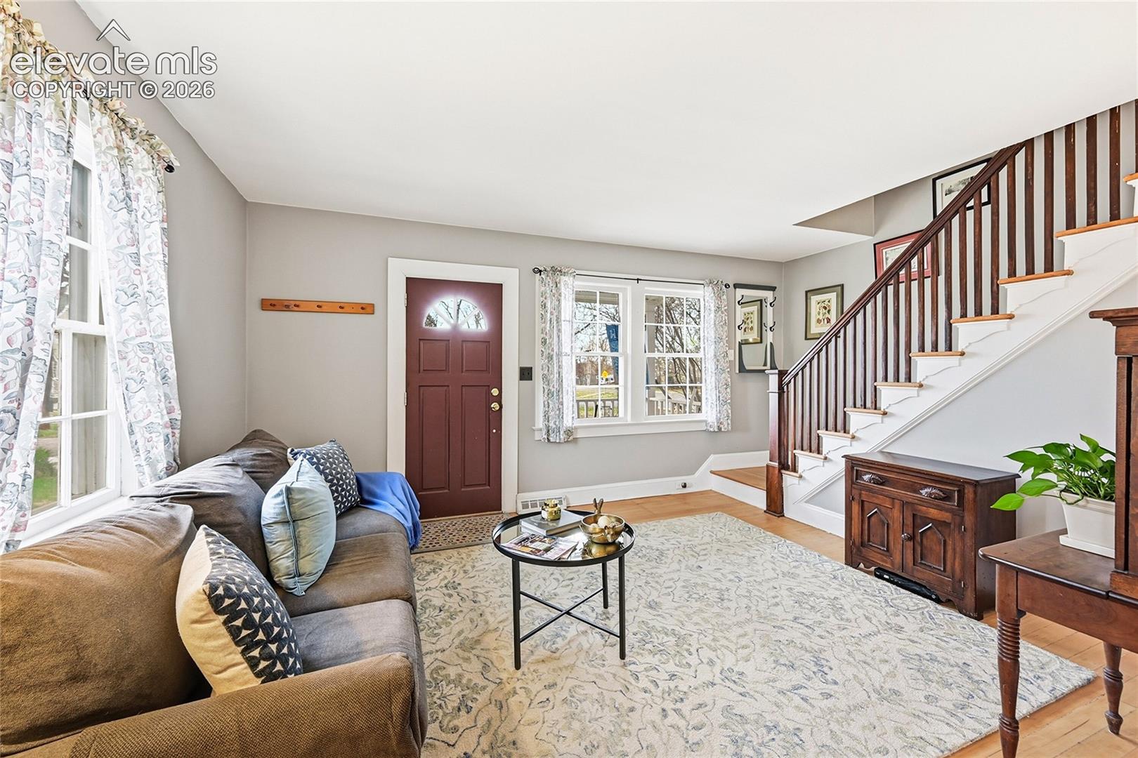 Entryway featuring wood-finish flooring, multi-pane windows, a paneled door with an arched glass inset, and a staircase with stained wood railings