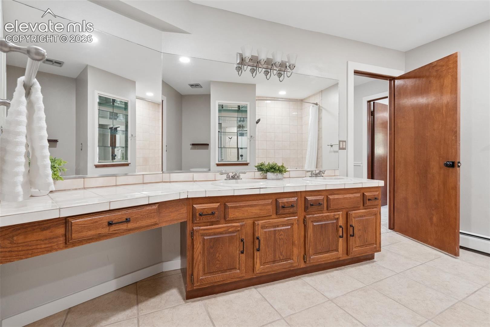 Expansive vanity with wood-finish cabinetry, dual undermount sinks, and tile countertop