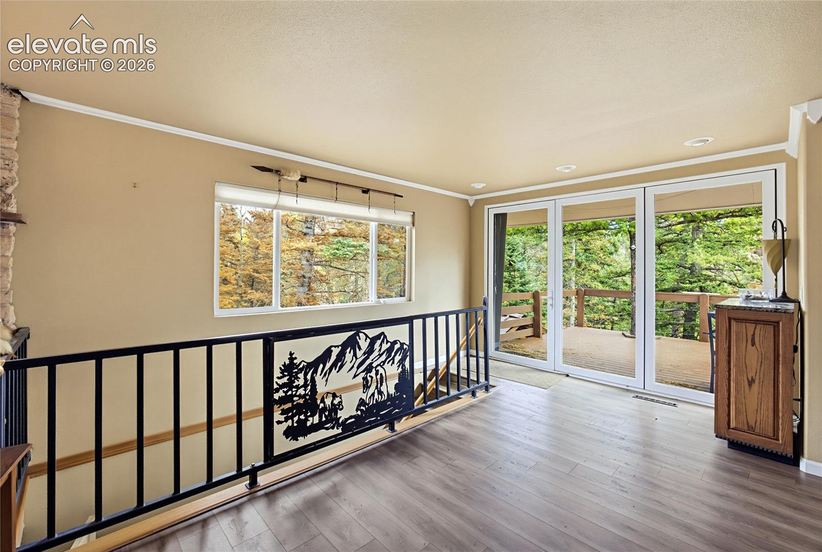 Wood-finish flooring, metal staircase railing with decorative mountain-themed panel, sliding glass doors, recessed lighting, and built-in cabinetry