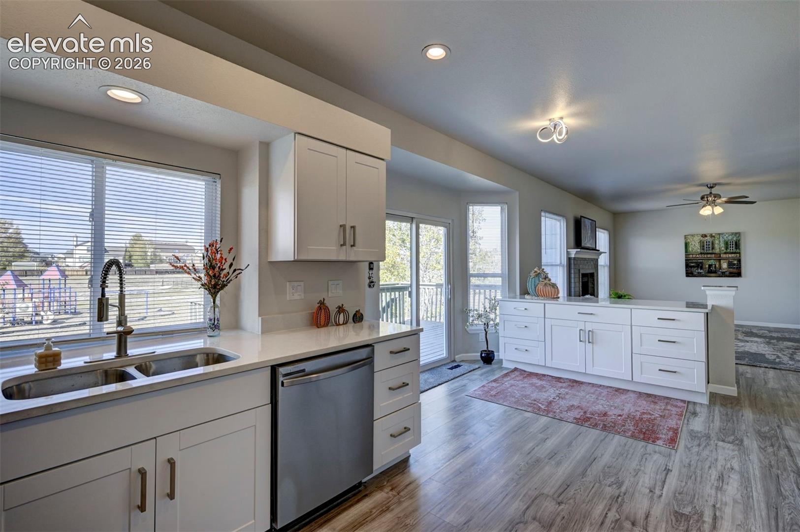 Kitchen featuring white shaker-style cabinetry, stainless steel appliances, quartz countertops, a dual-basin undermount sink with a high-arch faucet, and wood-finish flooring