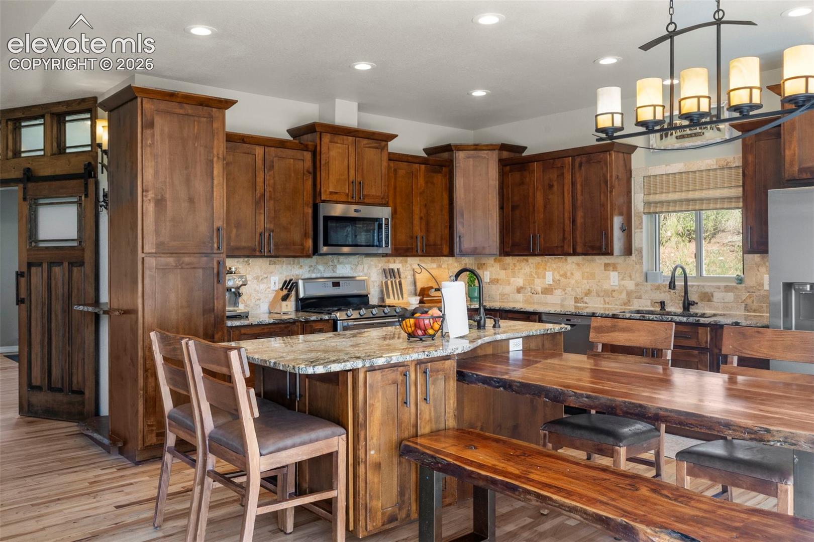 Kitchen with light stone counters, a barn door, stainless steel appliances, recessed lighting, and a center island with sink