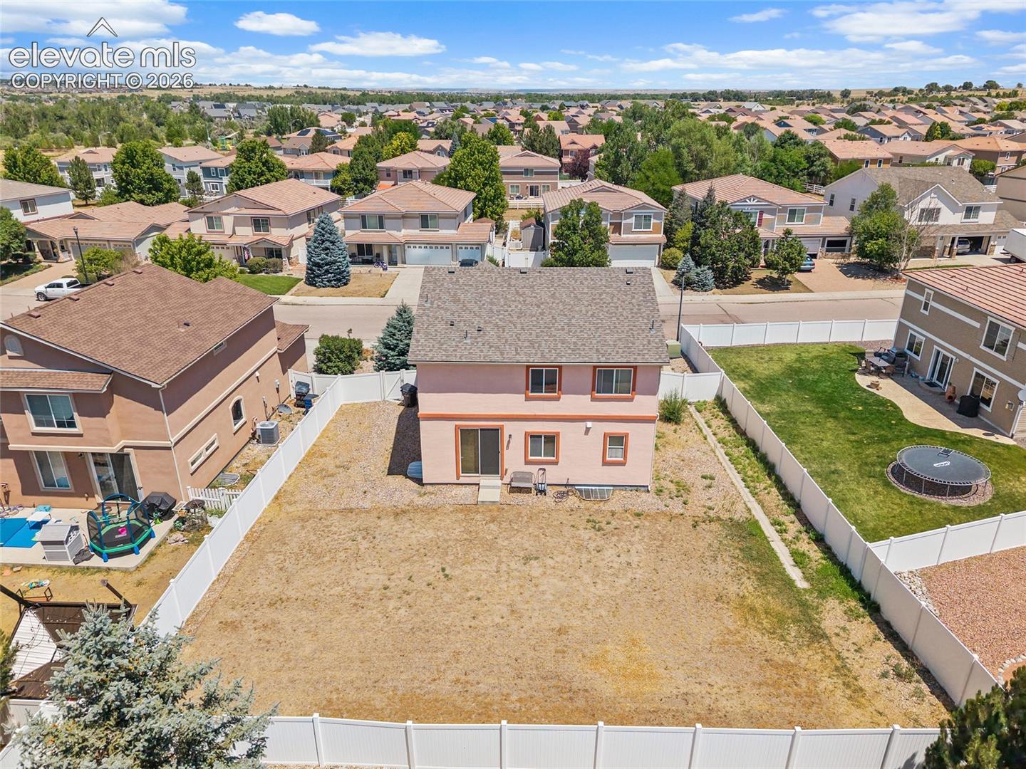 Two-story residence featuring a neutral-toned stucco exterior, a shingled roof, sliding glass patio doors, and a private, fully fenced backyard