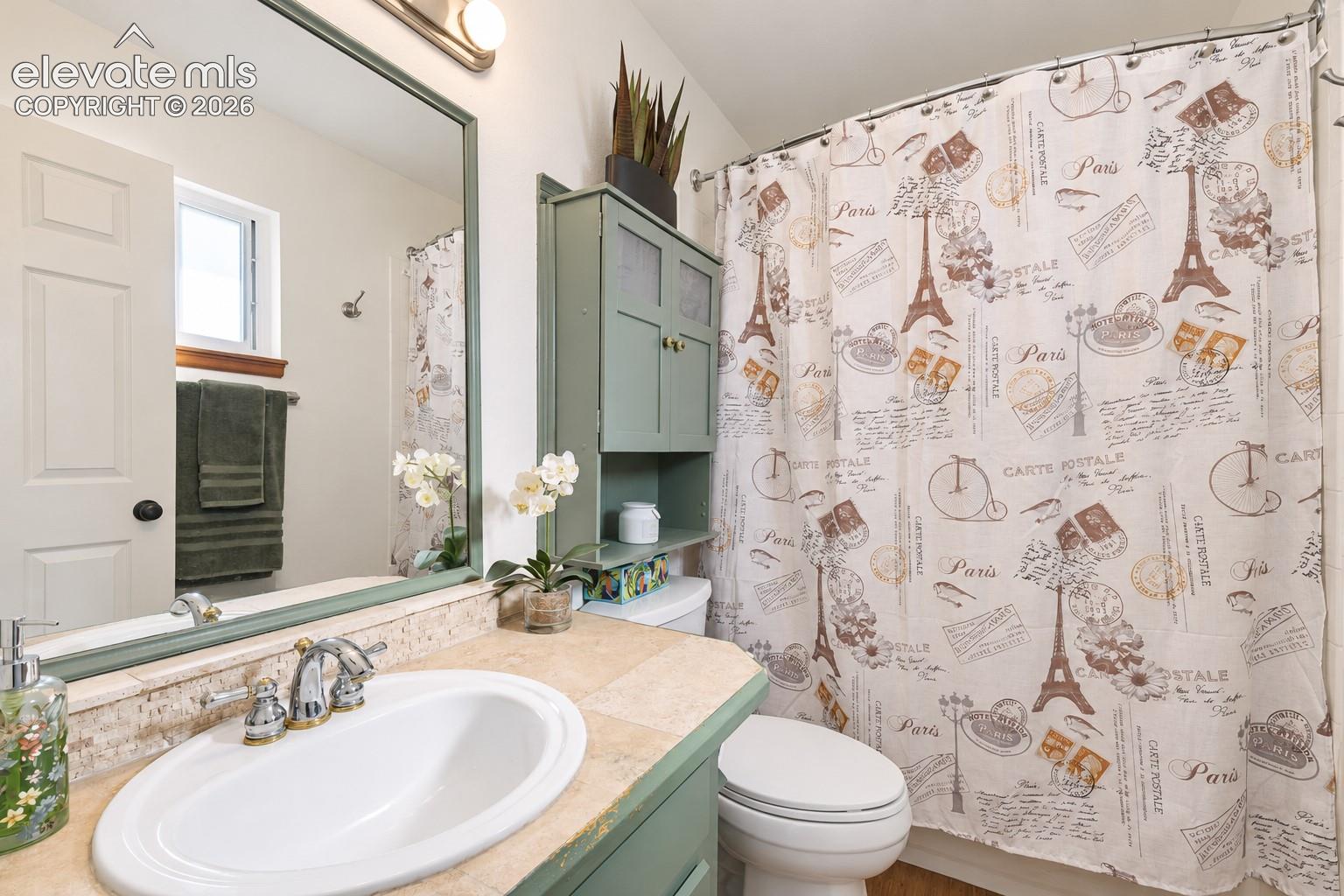 Bathroom featuring a stone-tile countertop, recessed vanity basin with polished chrome hardware, wall-mounted mirror with a color-coordinated frame, and built-in cabinet storage