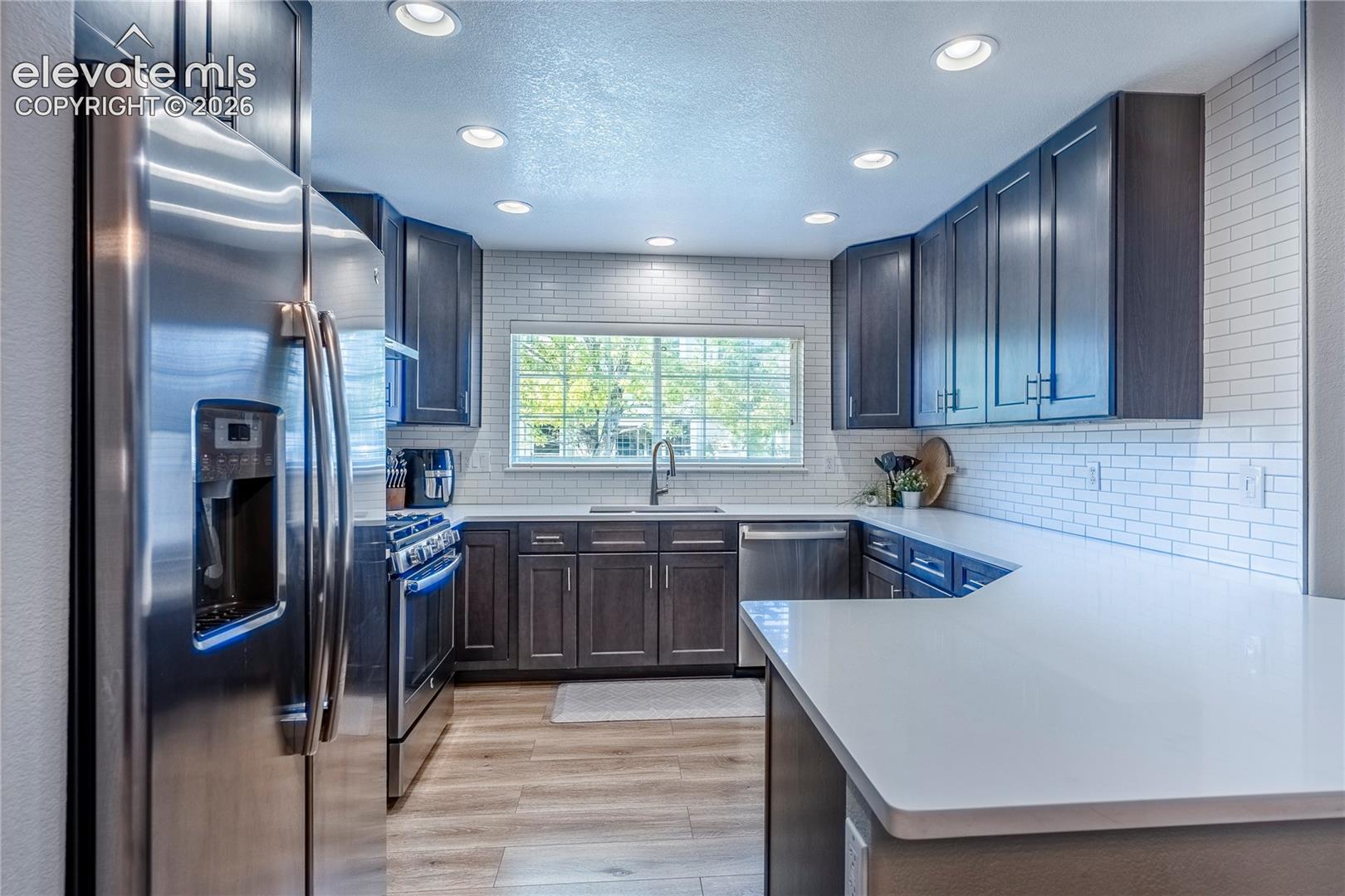 Kitchen featuring dark wood cabinetry, white countertops, stainless steel appliances, subway tile backsplash, and wood-finish flooring