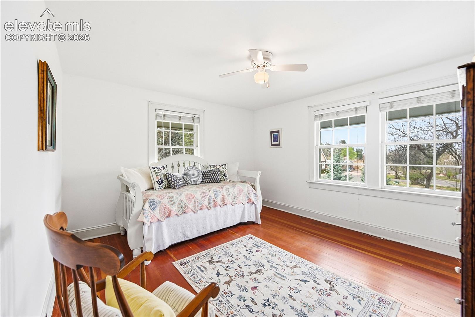 Room featuring wood-finish flooring, white walls, triple-pane windows with muntin dividers, and a ceiling fan with integrated lighting