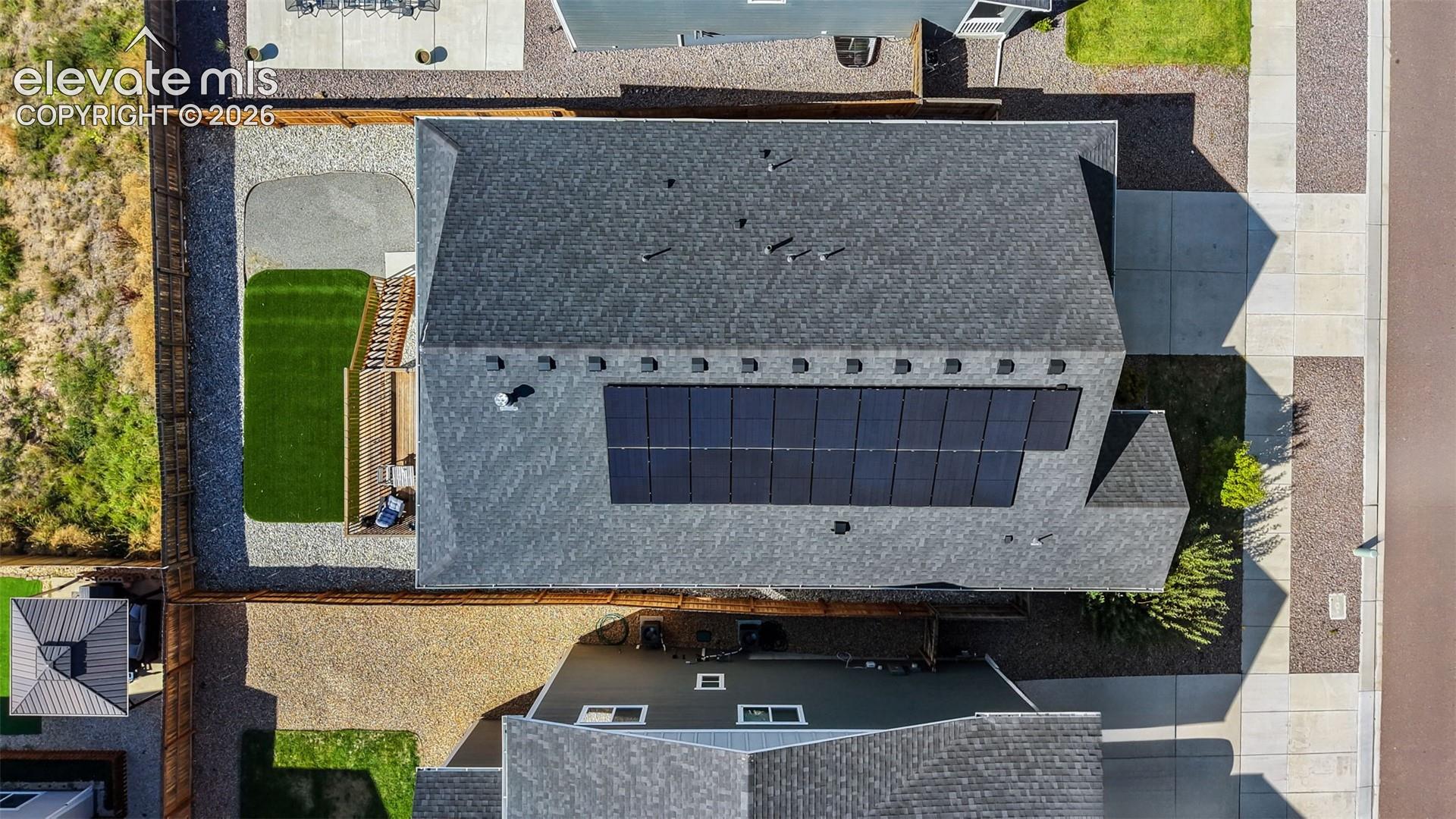 Shingled roof with integrated solar panels, fenced yard, gravel landscaping, and a manicured lawn area