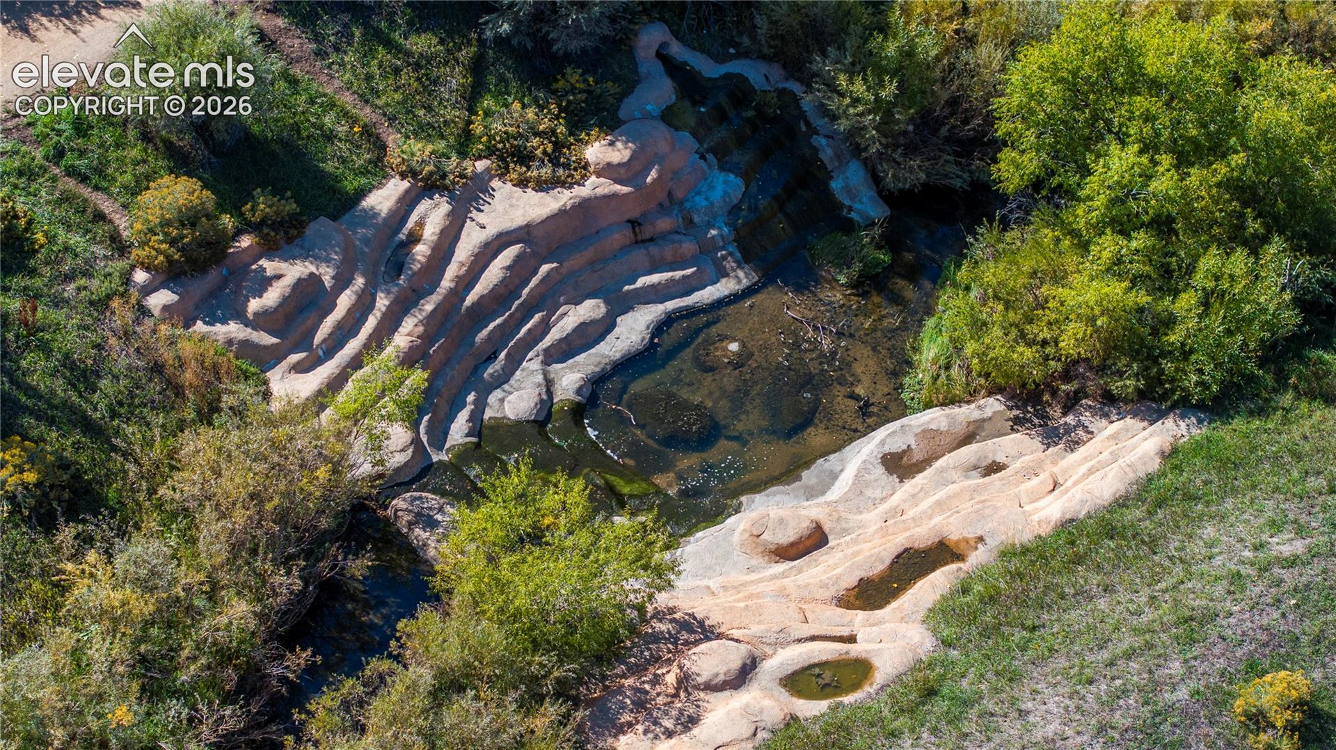 Natural rock formation featuring tiered stone basins, a cascading water feature, and mature trees