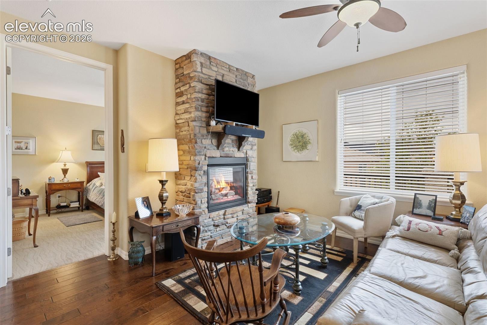 Living area featuring a floor-to-ceiling stone fireplace, hardwood flooring, and a ceiling fan