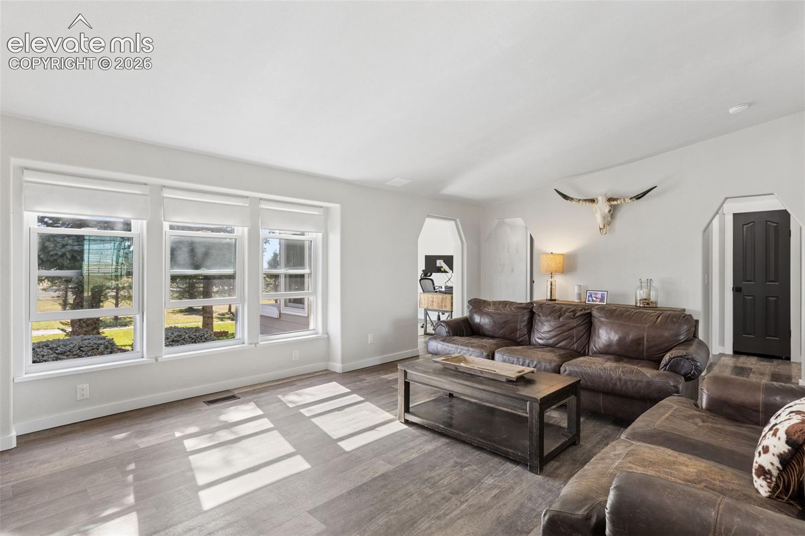 Living area featuring wood-finish flooring, multi-pane picture windows, neutral wall tones, and arched entryways