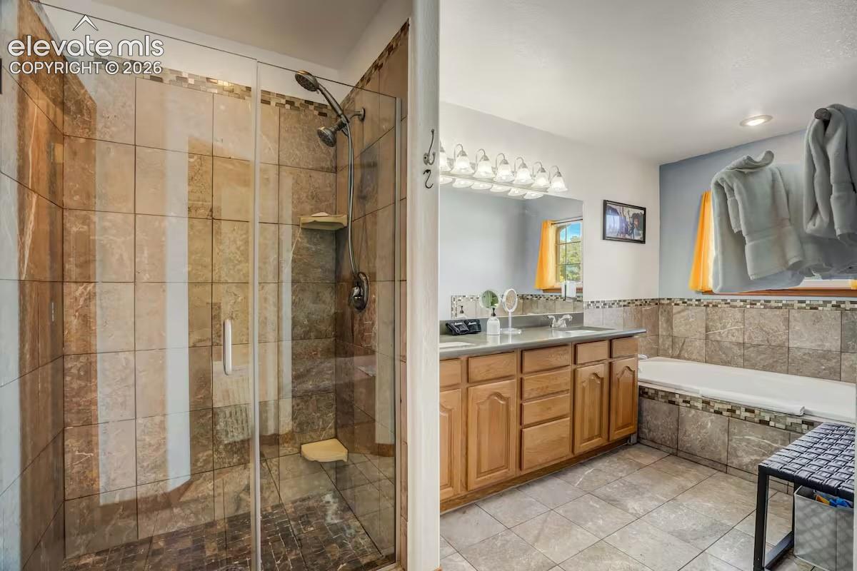 Spacious bathroom featuring a glass-enclosed shower with stone-look tile, a built-in shower bench, and a dual shower head system