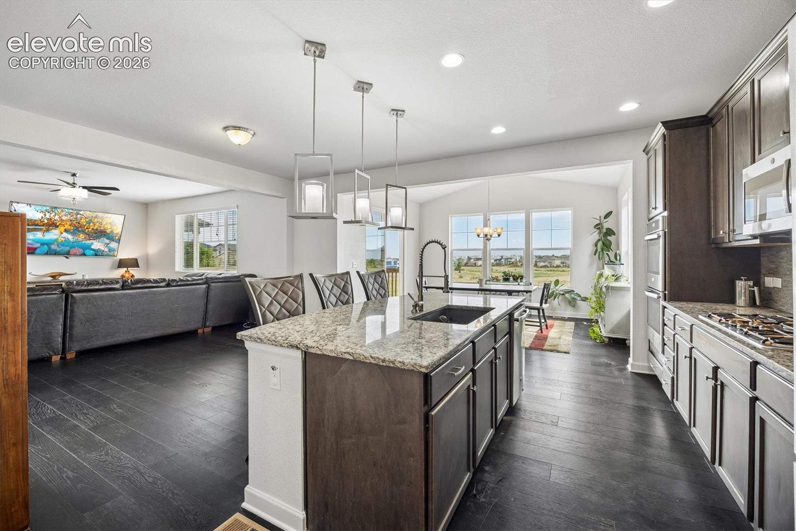 Kitchen featuring a large central island with seating, dark wood-finish flooring, recessed lighting, double ovens, and a gas cooktop