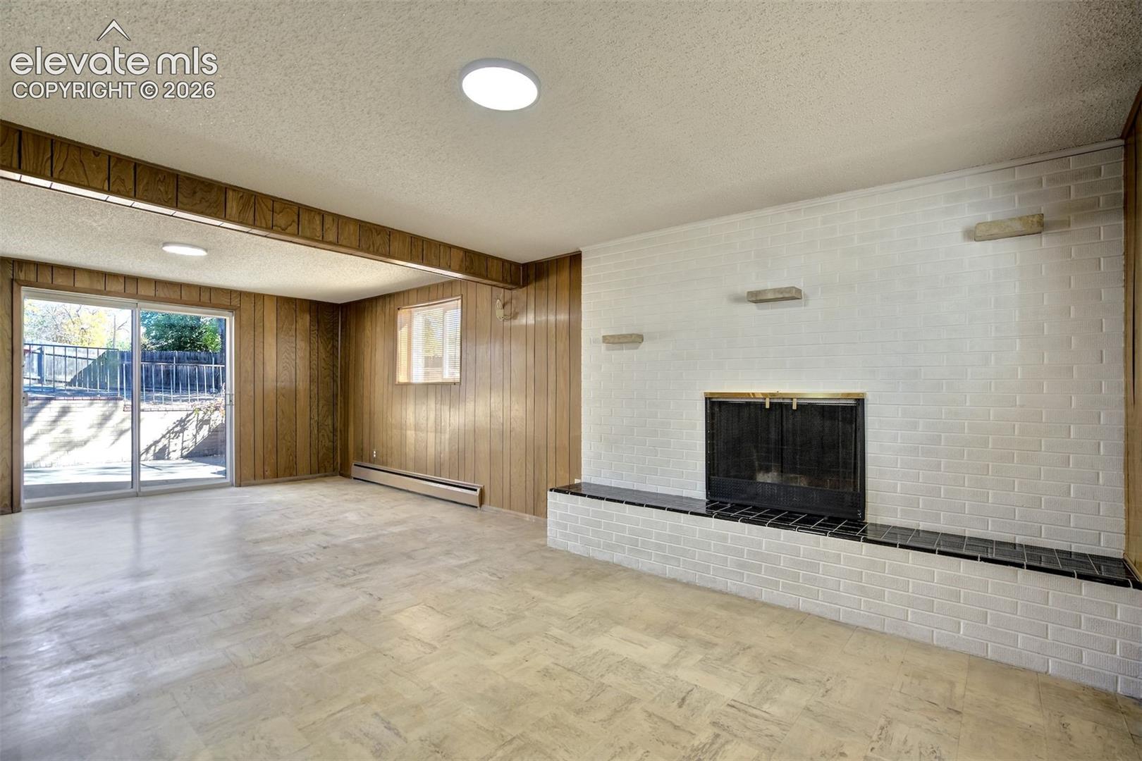 Fireplace featuring a white-painted brick surround and a black tiled hearth, accented by wood-paneled walls and a sliding glass door
