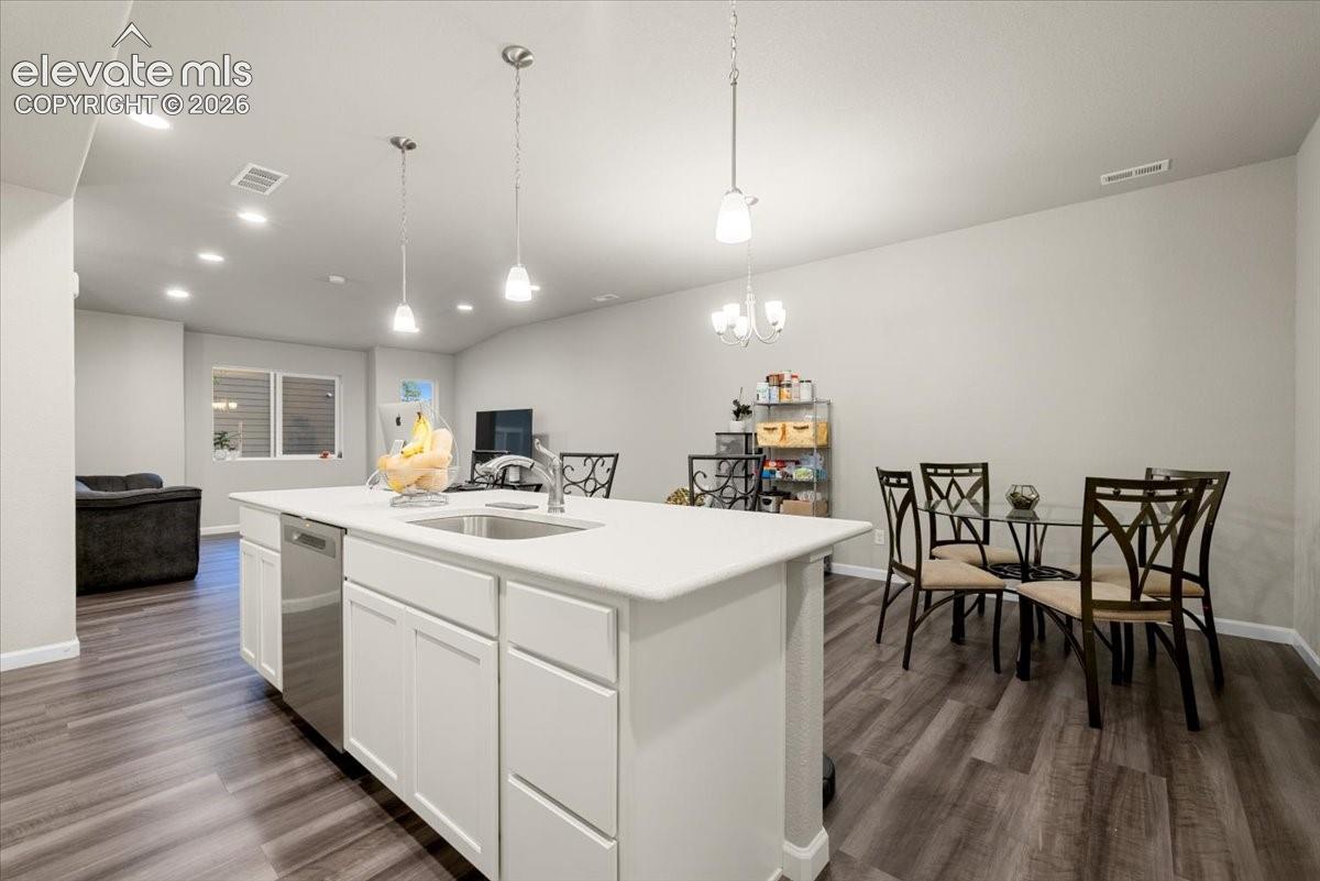 Open-concept living space with wood-finish flooring, recessed lighting, and an island featuring a stainless steel sink