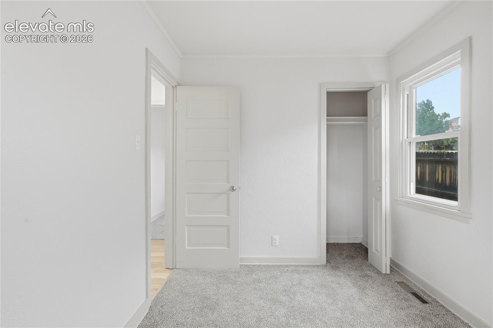 Neutral-toned interior space featuring light-colored wall paint, plush carpeting, a single-hung window, and an interior door with a five-panel design