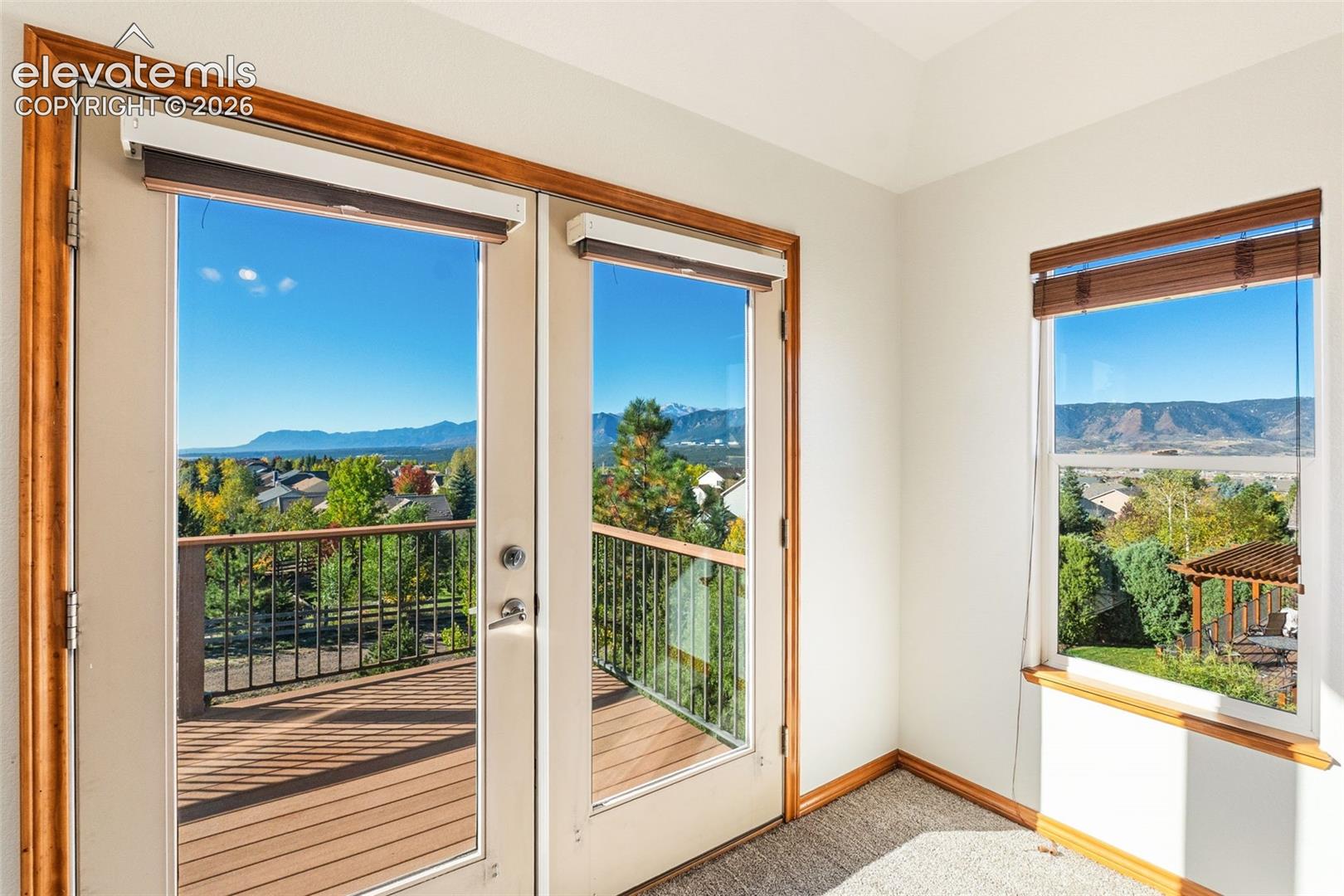 Double French doors with wood trim, exterior deck with metal railing, single-pane window with wood trim, and mountainous background scenery