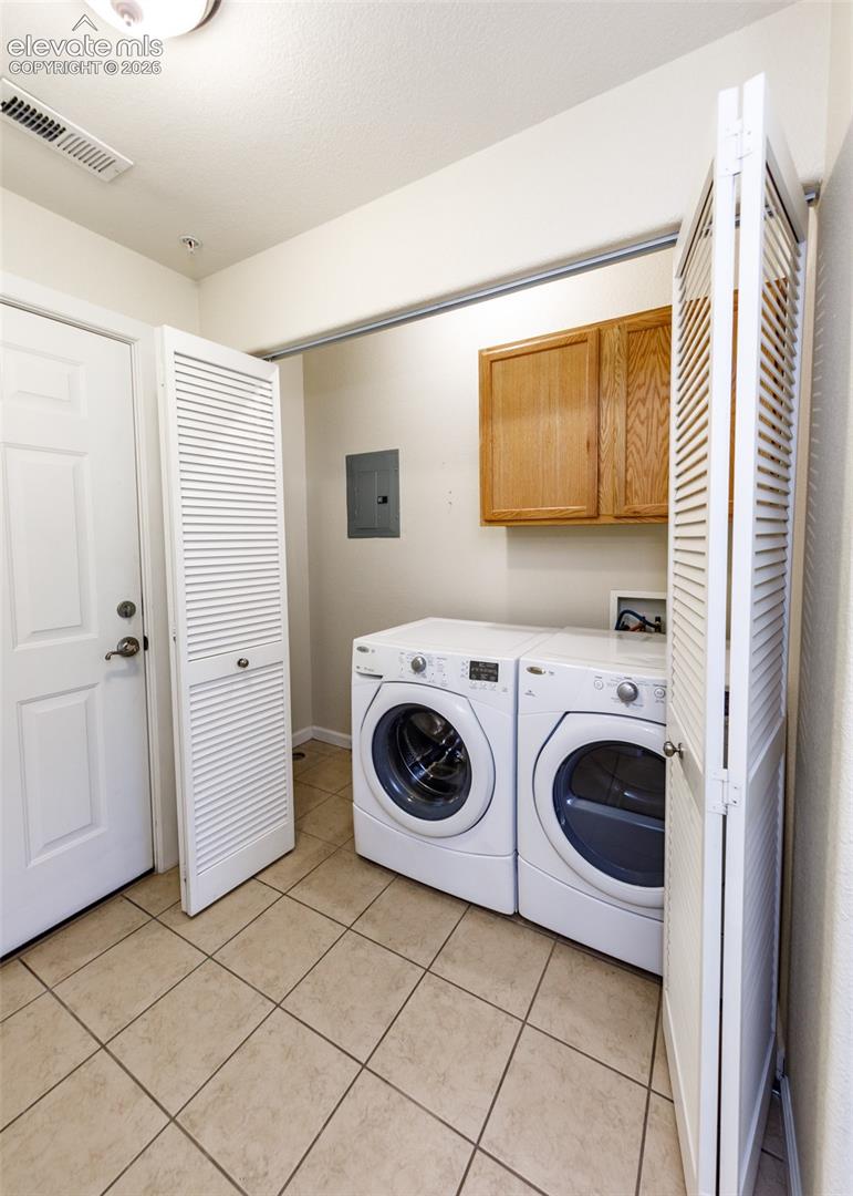 Utility space featuring ceramic tile flooring, built-in wooden cabinetry, and louvered folding doors