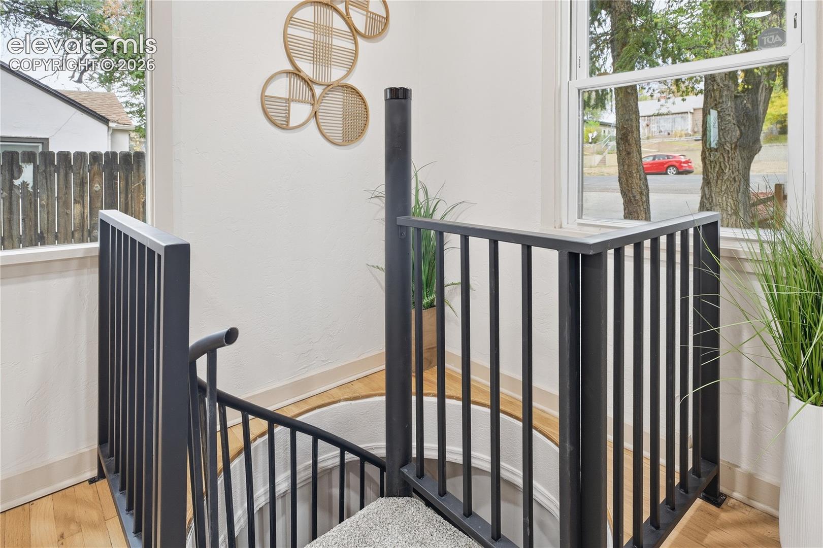 Spiral staircase with matte black metal railings, wood-finish flooring, and large windows