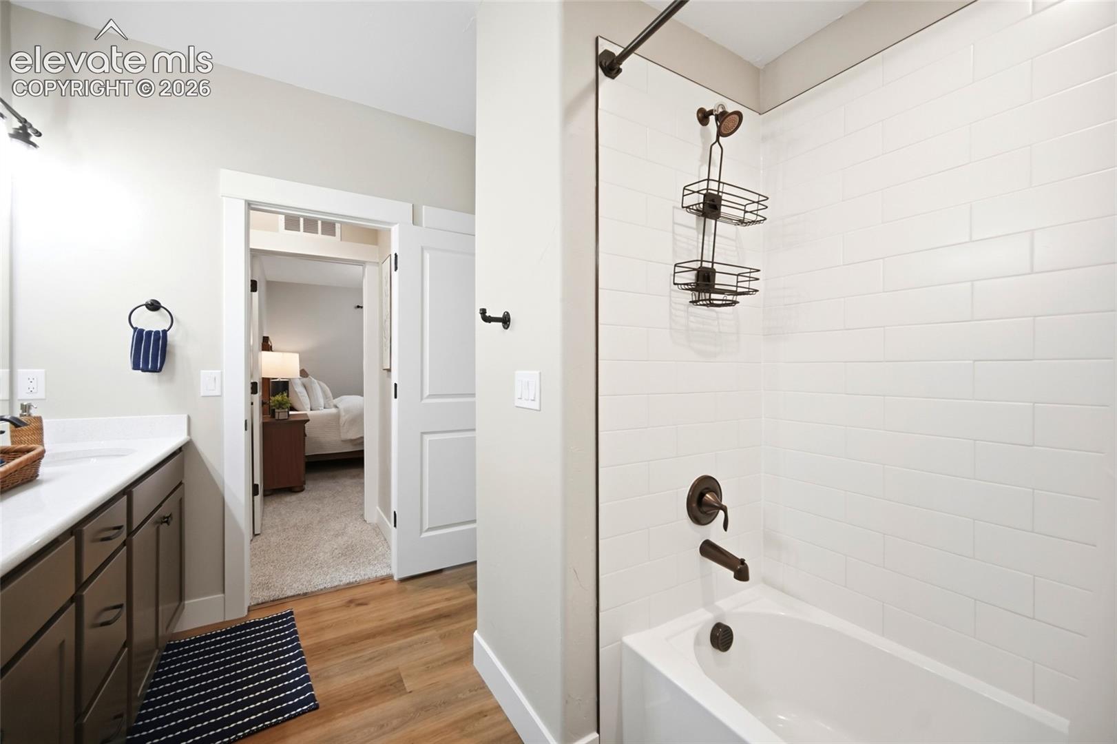 Bathroom featuring white subway tile surround, matte black fixtures, wood-finish flooring, and a white vanity with a neutral solid-surface countertop