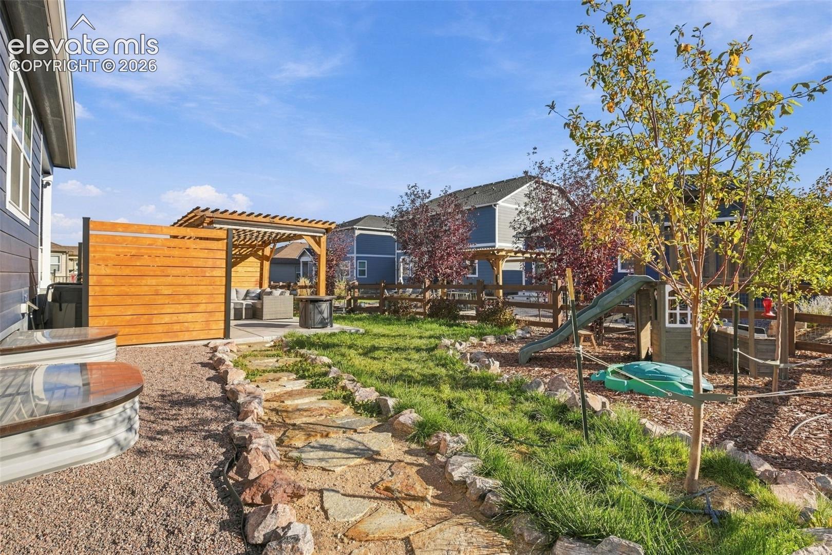 Backyard featuring a wood pergola, horizontal wood privacy fencing, a natural stone path, rock landscaping, and metal window wells
