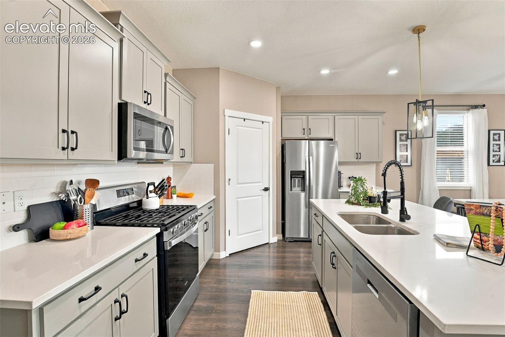 Kitchen featuring grey shaker-style cabinetry, quartz countertops, subway tile backsplash, stainless steel appliances, and a central island with an undermount dual-basin sink