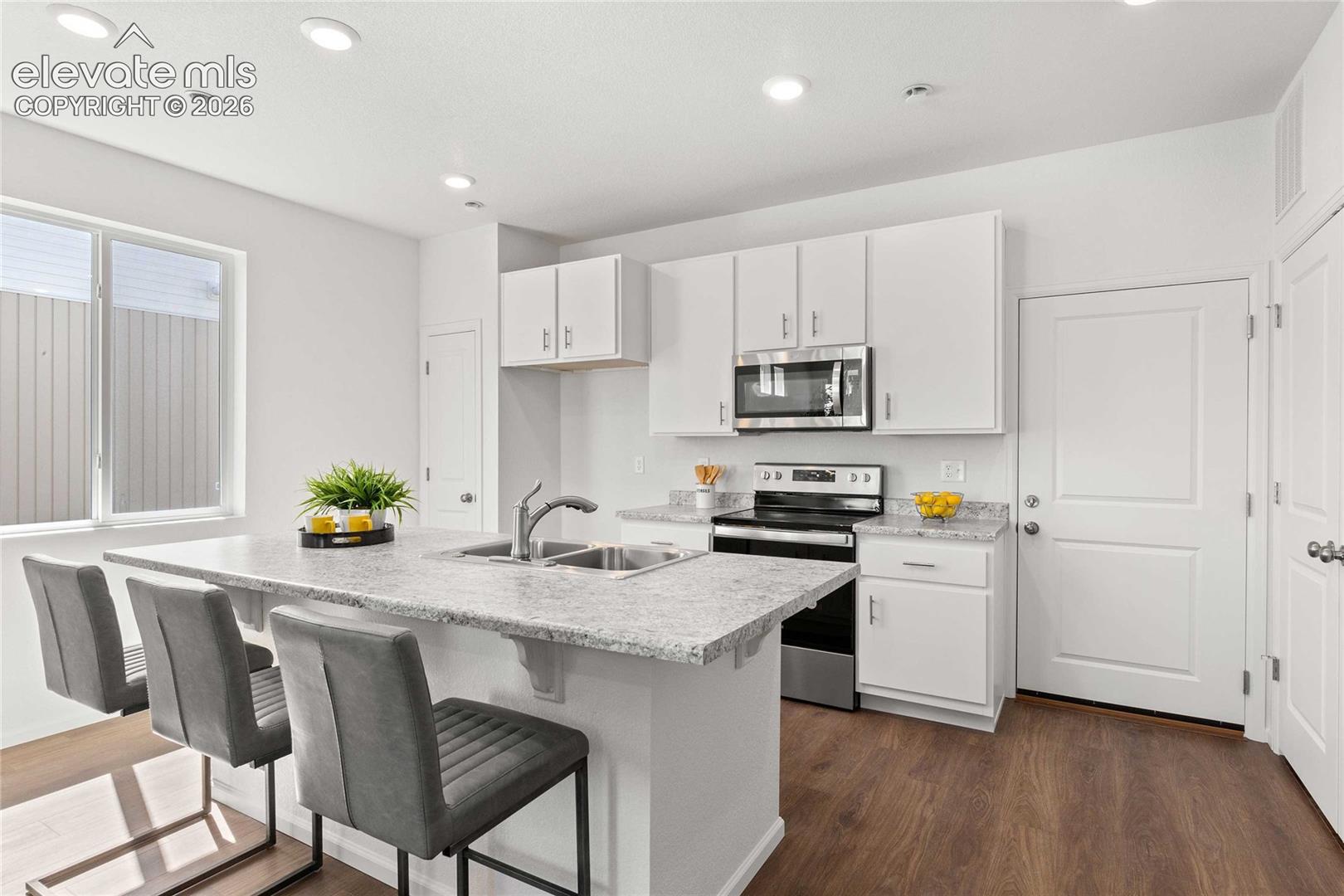 Kitchen featuring white cabinetry, stainless steel appliances, a double basin sink, light-toned countertops, and wood-finish flooring
*photos  of a model home*
