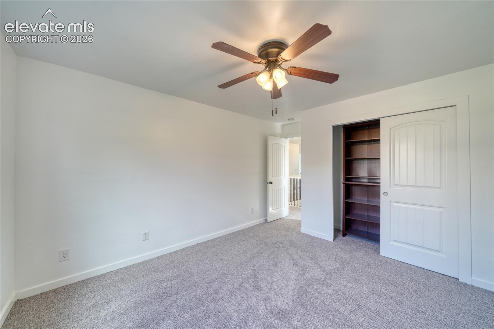 Carpeted room featuring a ceiling fan with integrated lighting, a built-in bookshelf, and a sliding panel door closet