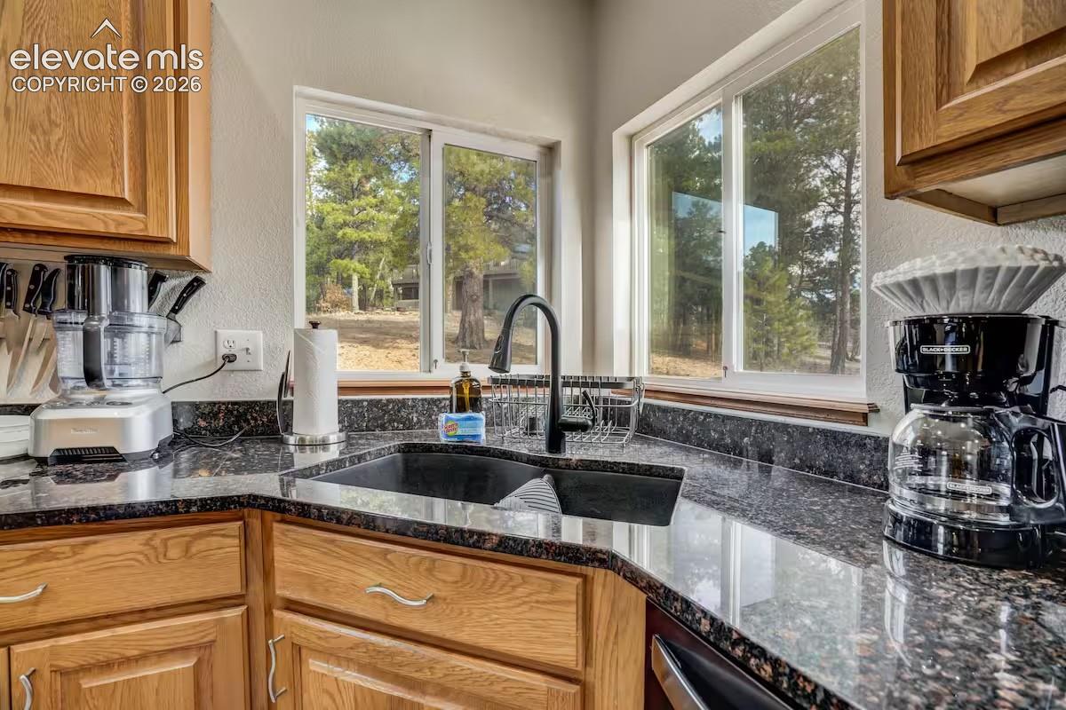 Kitchen featuring wood cabinetry, dark granite countertops, a black double-basin sink, and a modern black faucet