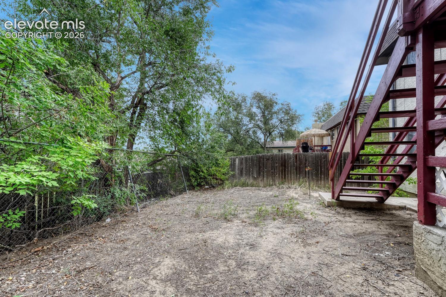 Expansive outdoor space featuring a solid wood privacy fence, chain link fencing, and mature trees