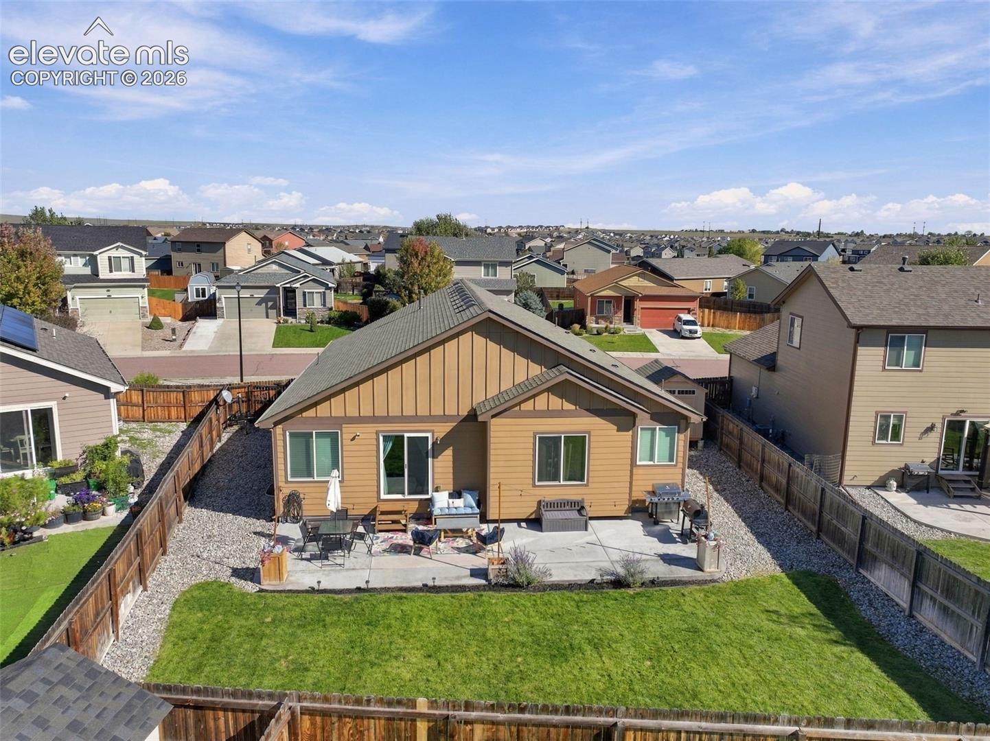 Rear exterior featuring vertical and horizontal siding, an expansive concrete patio, a fenced backyard, and a manicured lawn