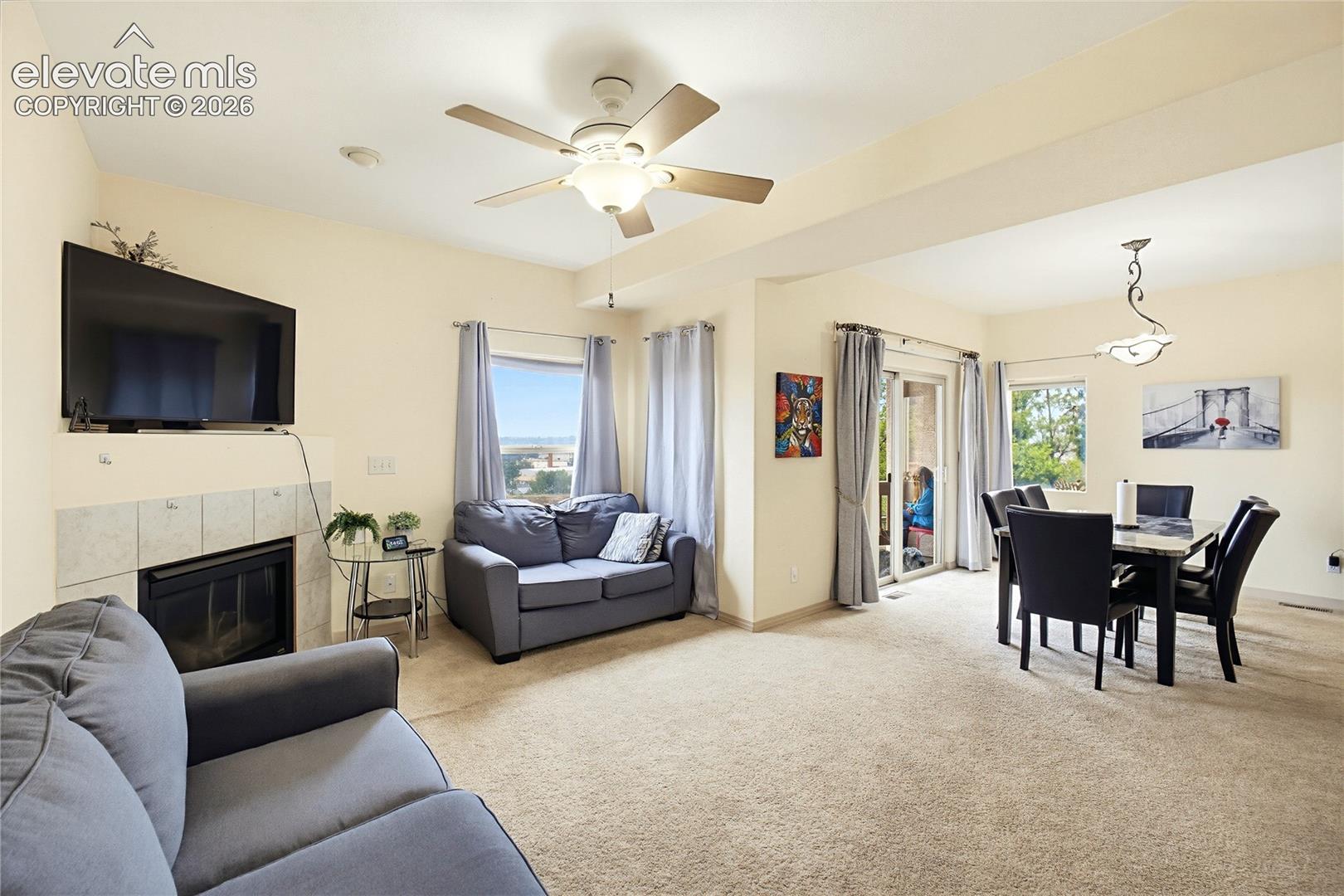 Open-concept living space with a tiled fireplace, ceiling fan, and carpeted flooring