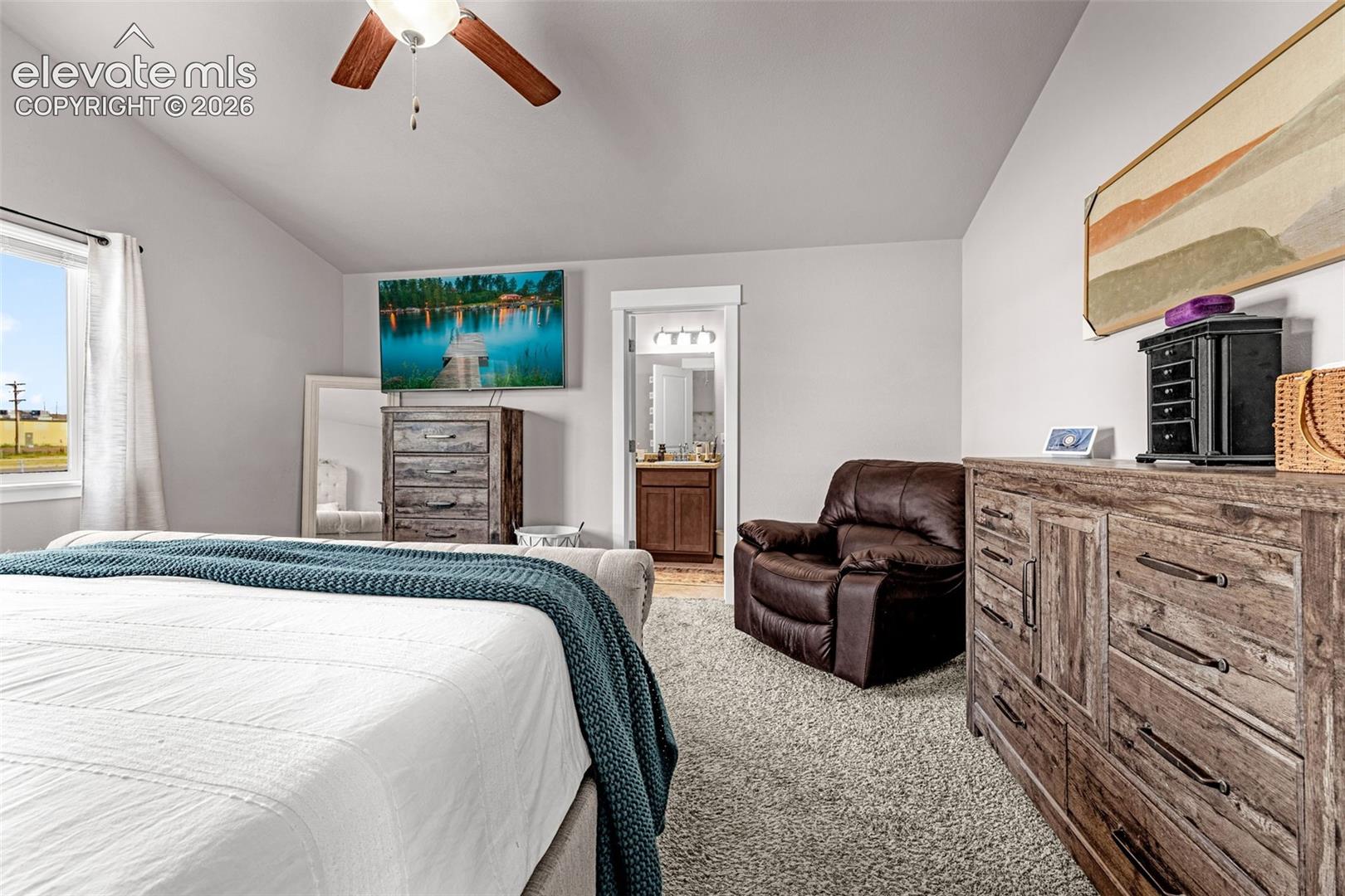 Vaulted ceiling bedroom featuring a ceiling fan, a window with exterior views, and an entryway to an attached bathroom