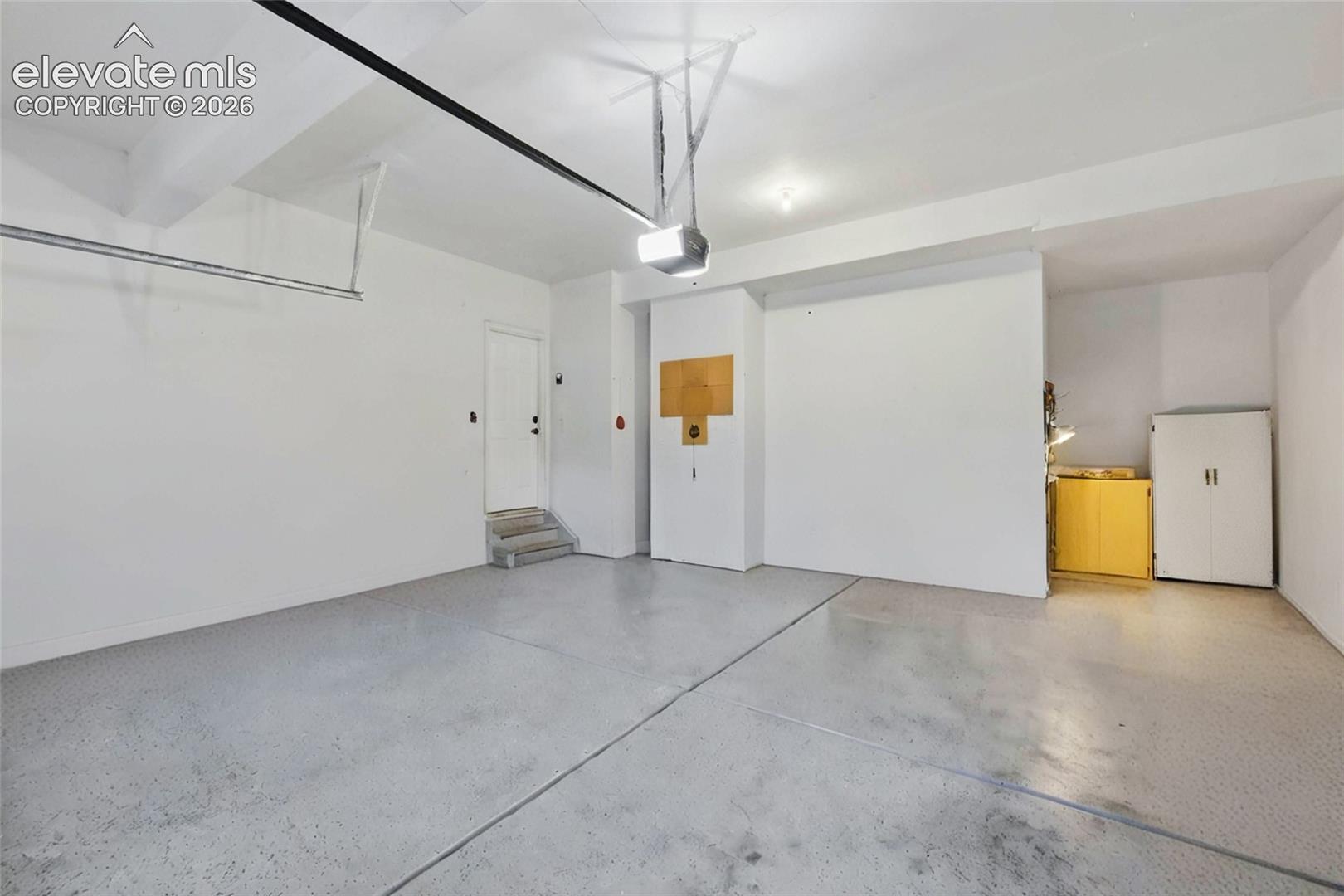 Spacious, oversized garage featuring epoxied concrete flooring and white walls